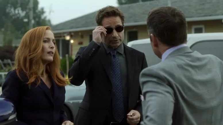 Two FBI agents from a sci-fi series investigating paranormal cases standing outdoors near a vehicle in a suburban area.