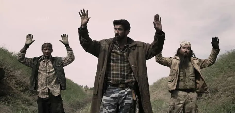 Post-apocalyptic horror series scene showing survivors raising hands during a tense zombie outbreak moment in the United States.
