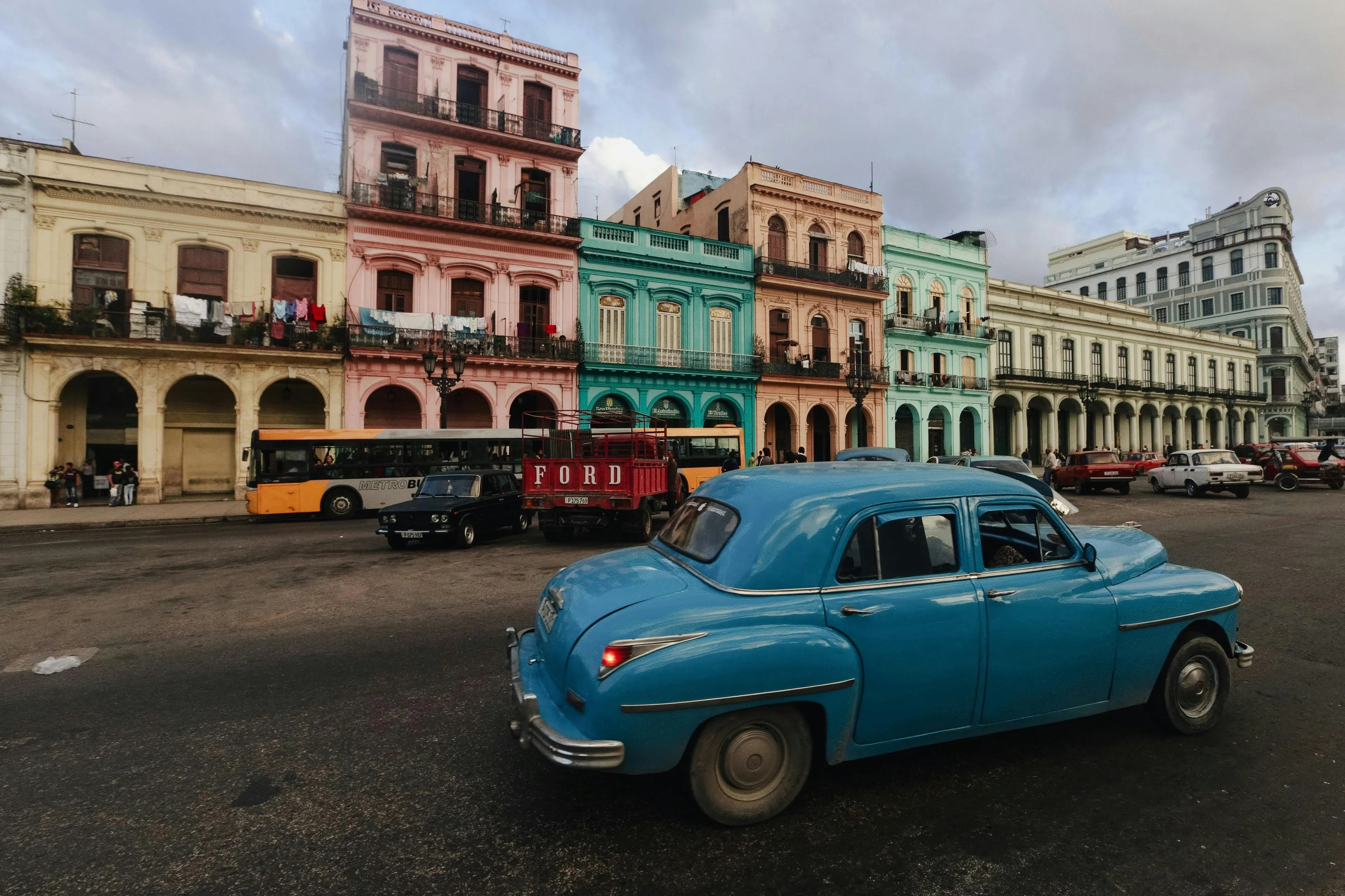 Vintage blue car driving past colorful colonial buildings in a Caribbean city street scene for guess the Caribbean country.