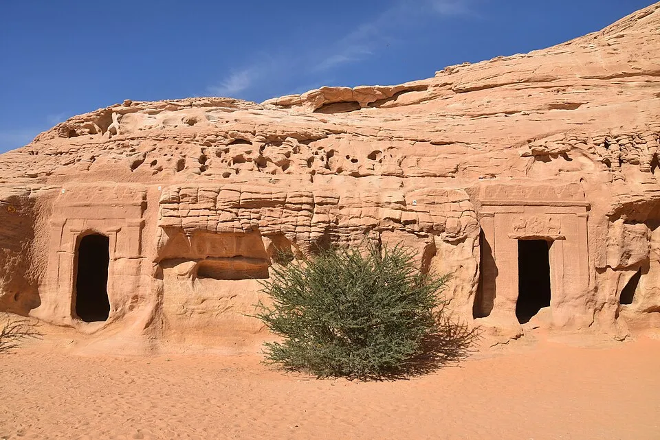 Ancient rock-cut tombs in desert landscape with clear blue sky, a challenging guess of countries from a single picture.