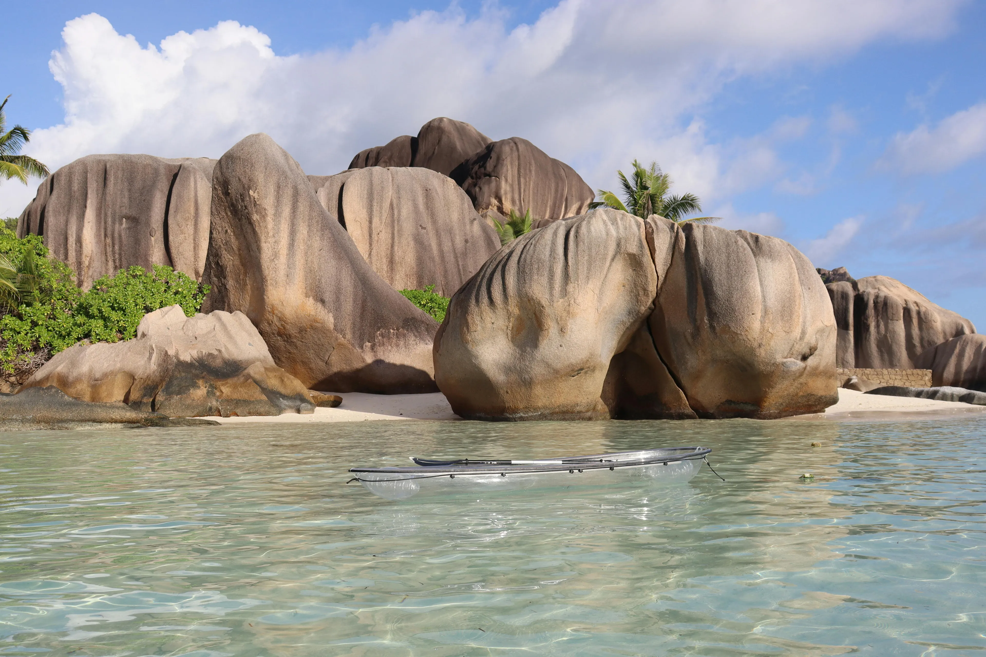 Clear water with a transparent kayak near large smooth rocks on a tropical beach in an island country.