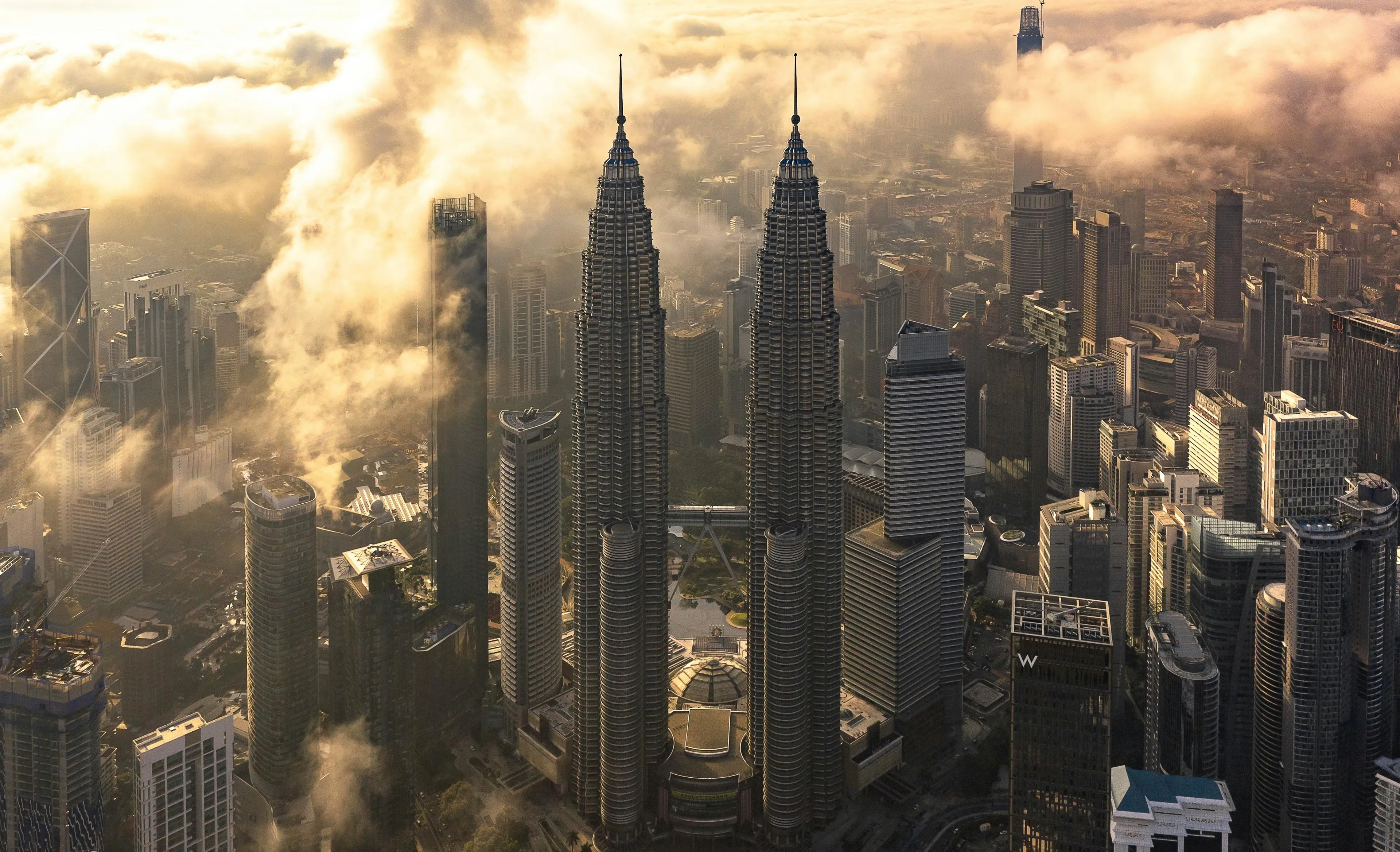 Aerial view of Kuala Lumpur cityscape with Petronas Towers surrounded by clouds in Southeast Asian country.