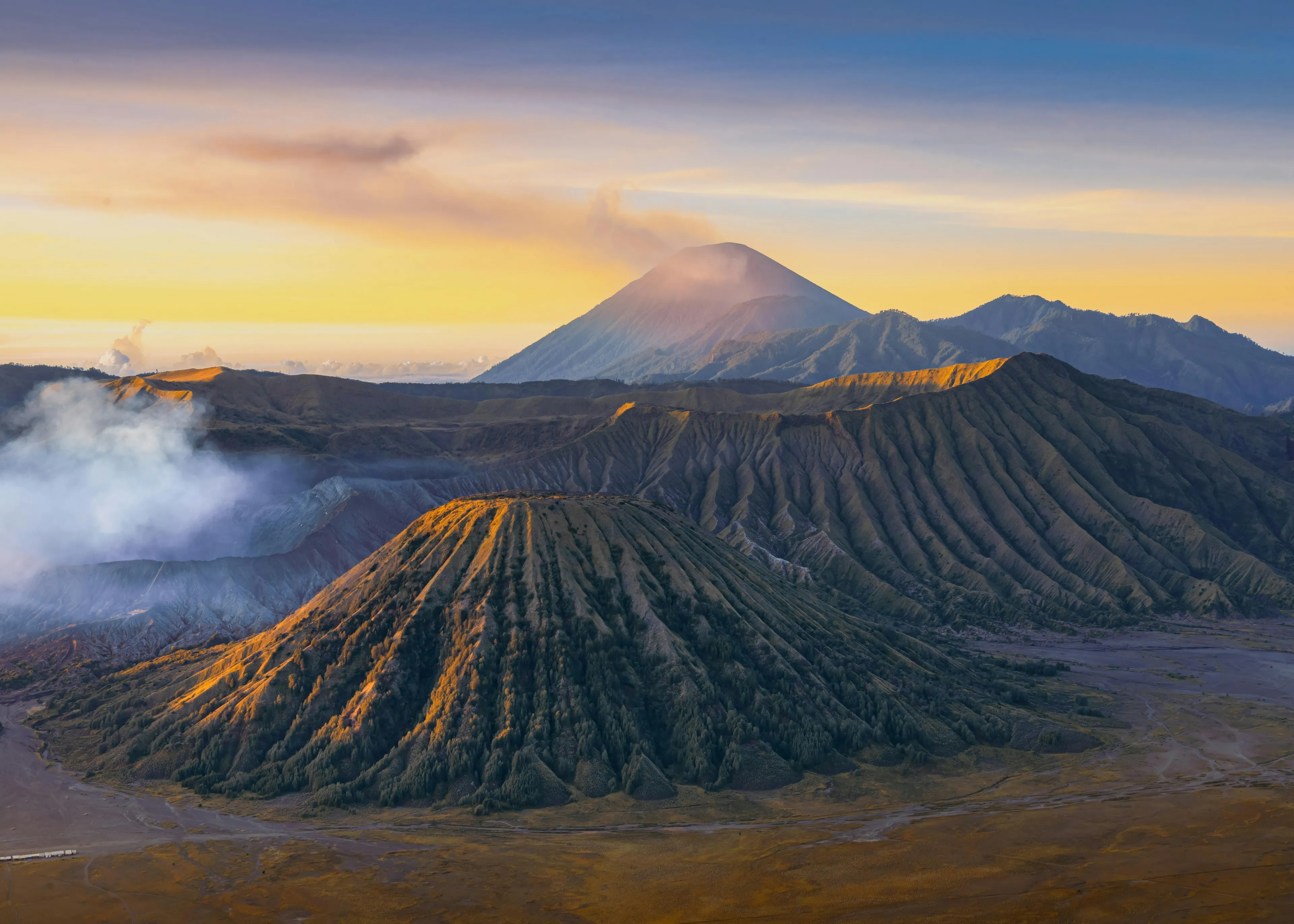 Aerial view of volcanic mountains at sunrise in a Southeast Asian country with smoky crater and rugged terrain.