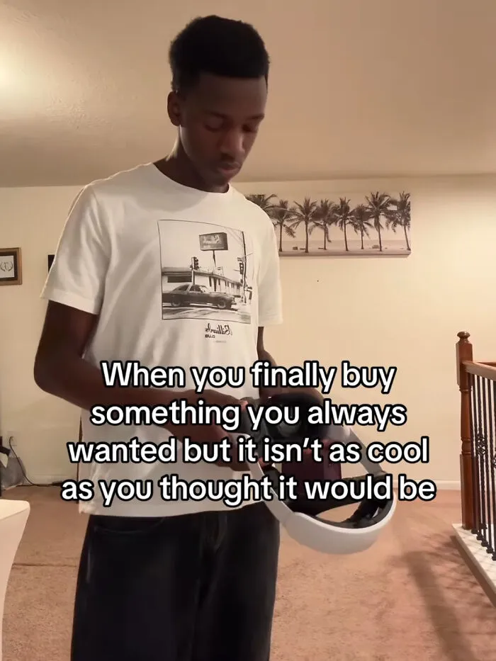 Young man holding a helmet with a relatable funny meme about buying something not as cool as expected indoors.