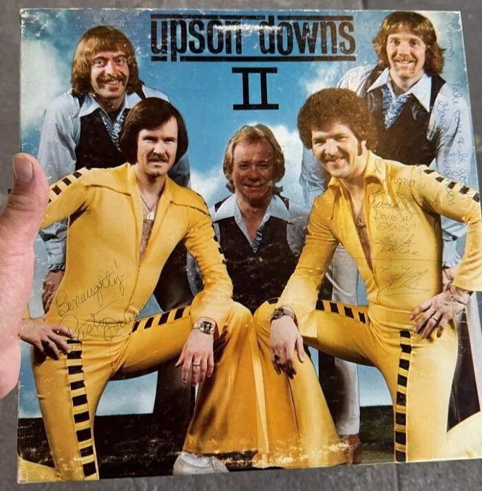 Vintage band posing on a hilariously bad album cover wearing yellow jumpsuits with 1970s hairstyles and fashion.