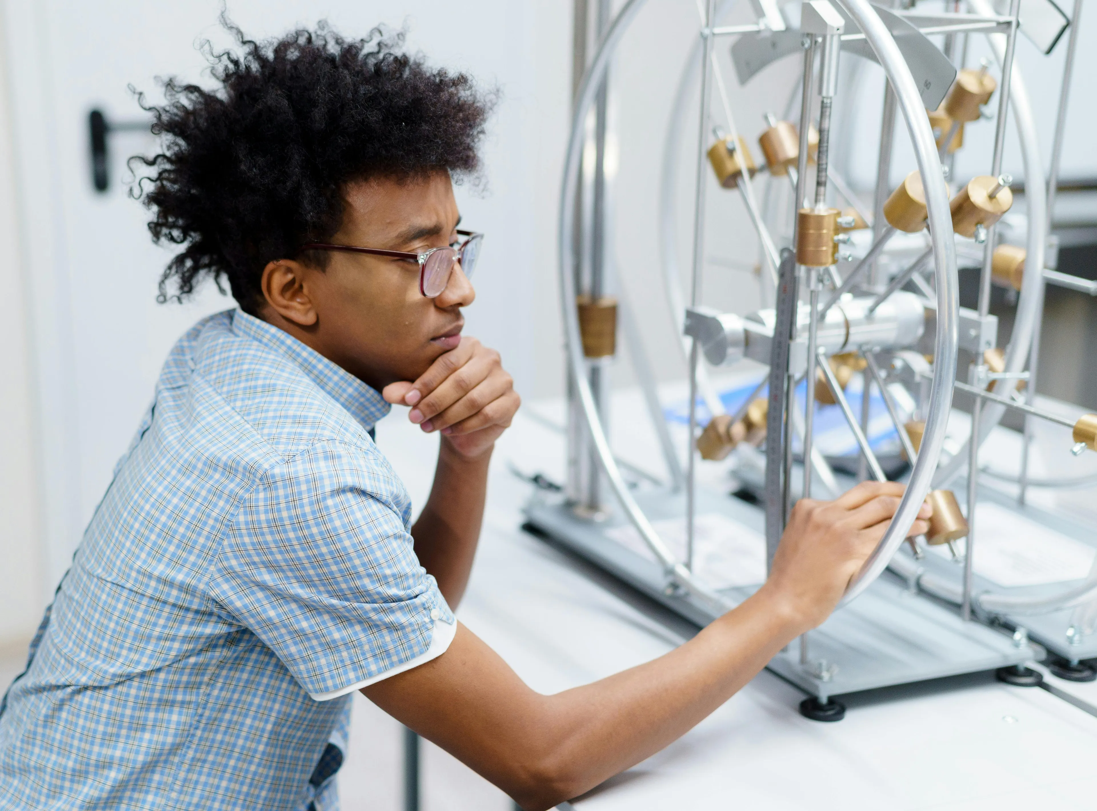 Teenage student in glasses studying science experiment equipment focused on defining resistance in a classroom setting.