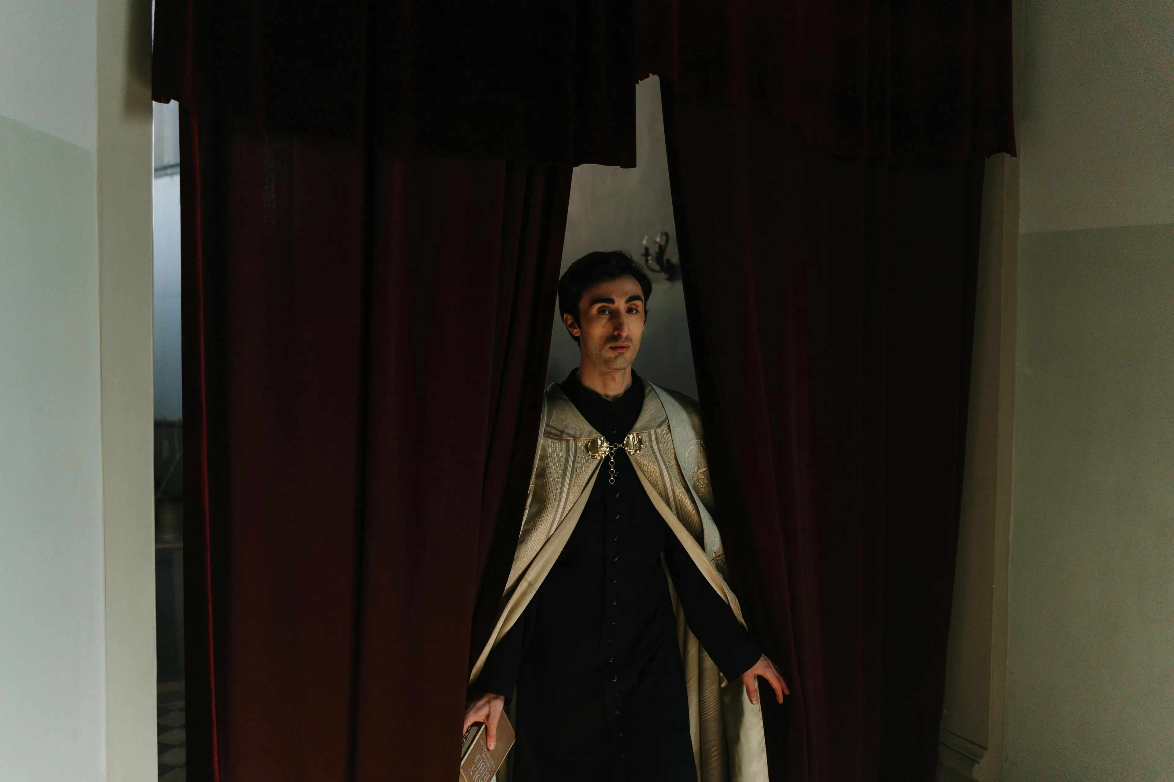Young man in a dark cloak stands between curtains, symbolizing themes of ambition and guilt in Shakespeare’s Macbeth literature.