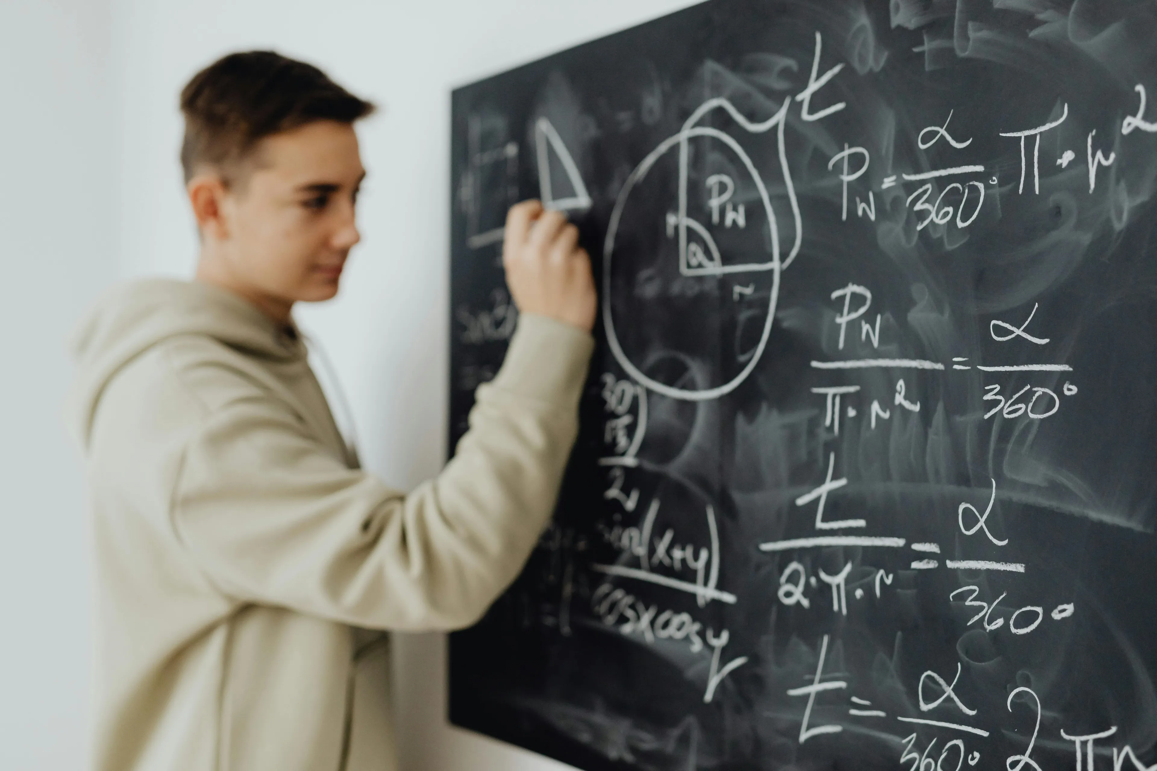 Teenager solving math problems on a chalkboard, focusing on circle radius and area calculations in a classroom setting.