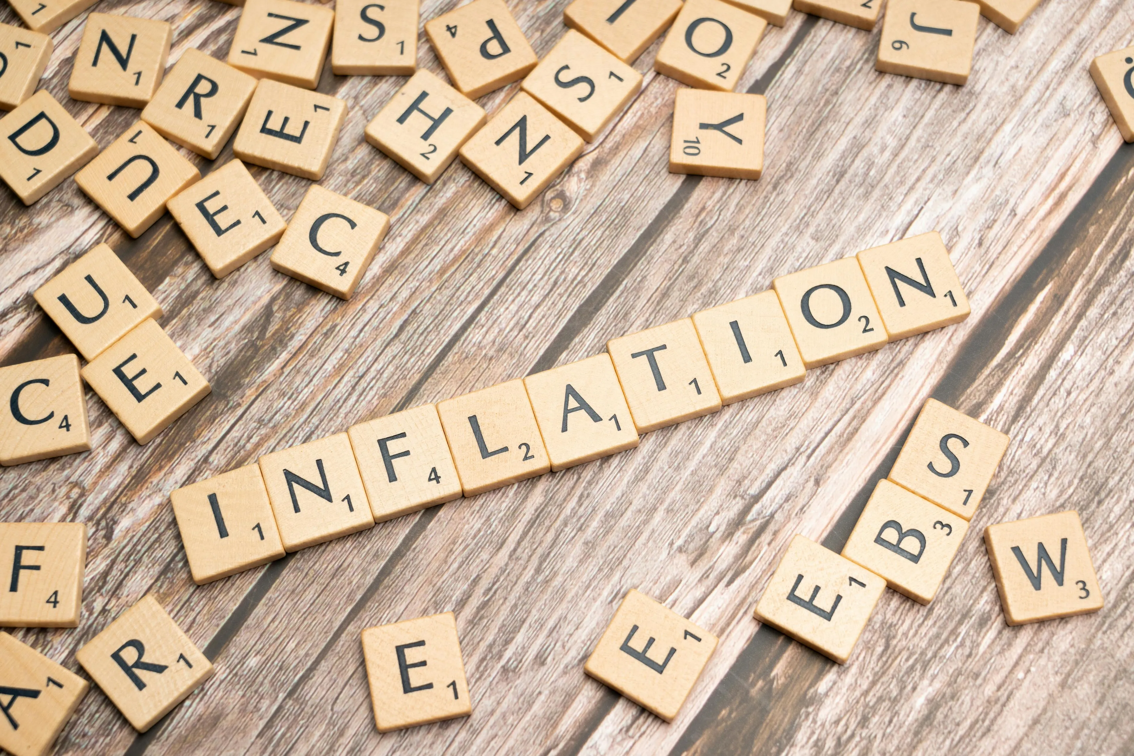 Scrabble tiles spelling inflation on a wooden table, illustrating economics and impact of rising inflation.