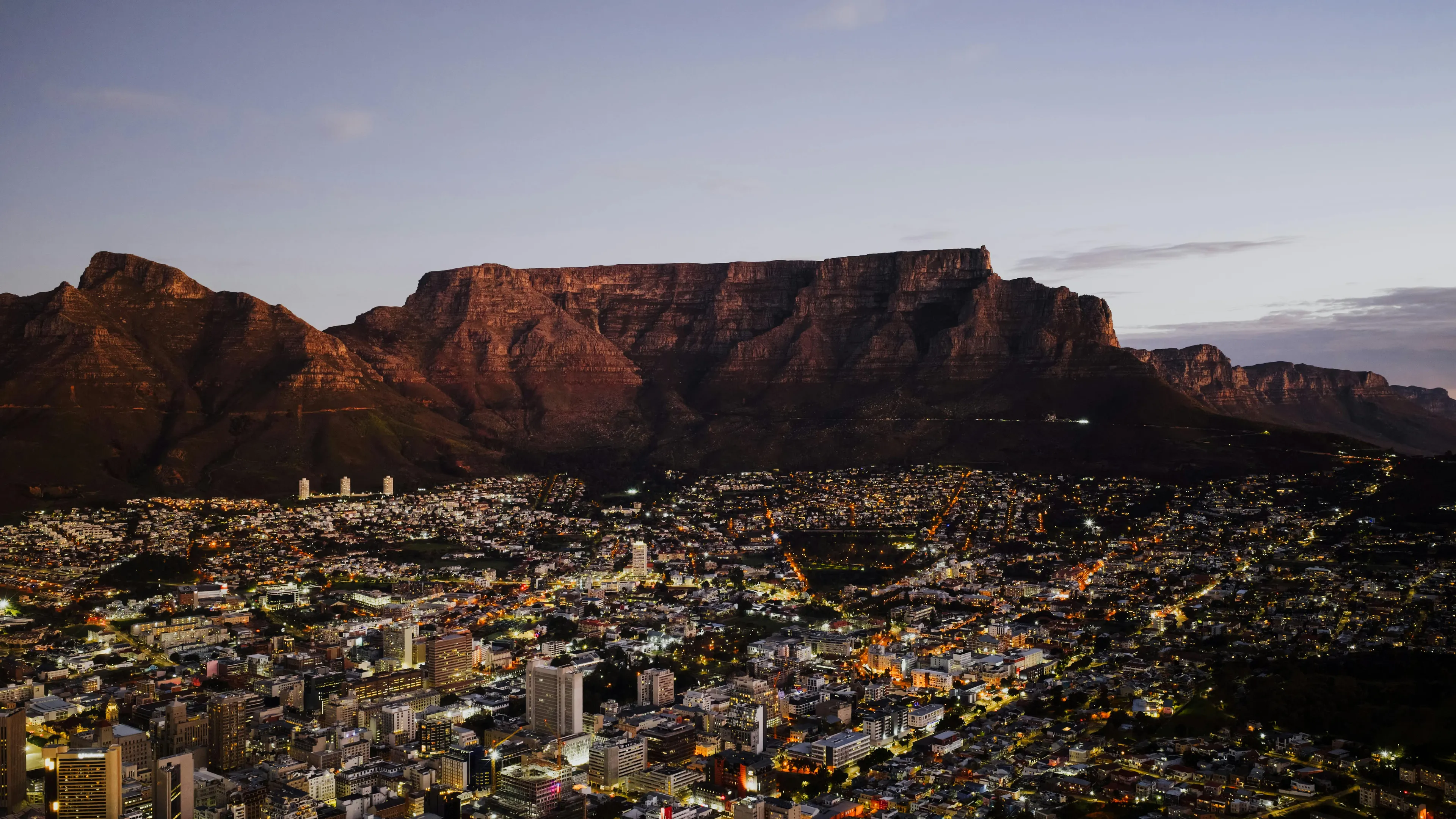 South Africa cityscape at dusk with Table Mountain in the background under a clear sky.