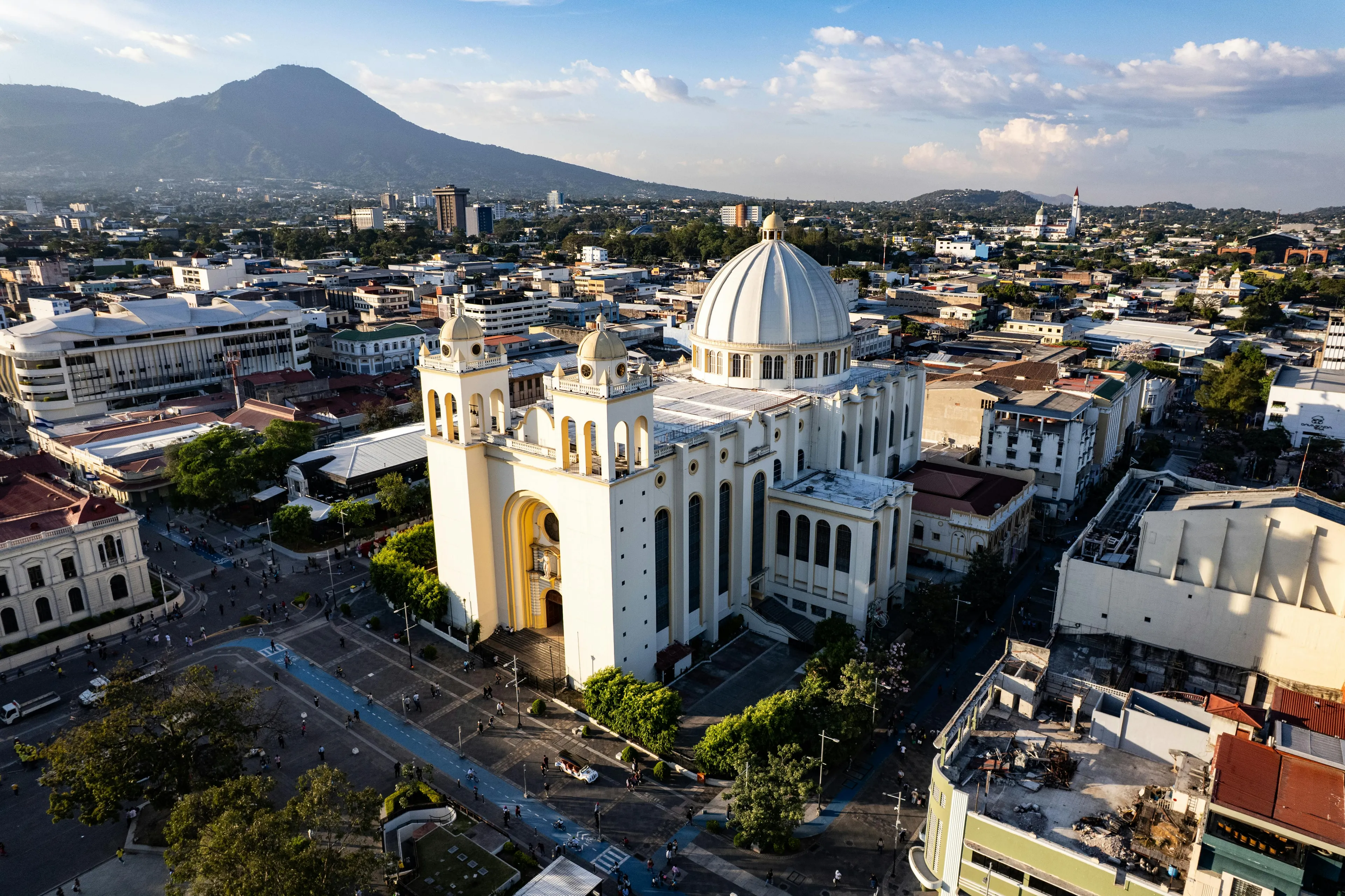 Aerial view of a cathedral with a dome in El Salvador, known as the Land of Volcanoes, with cityscape and mountains behind.
