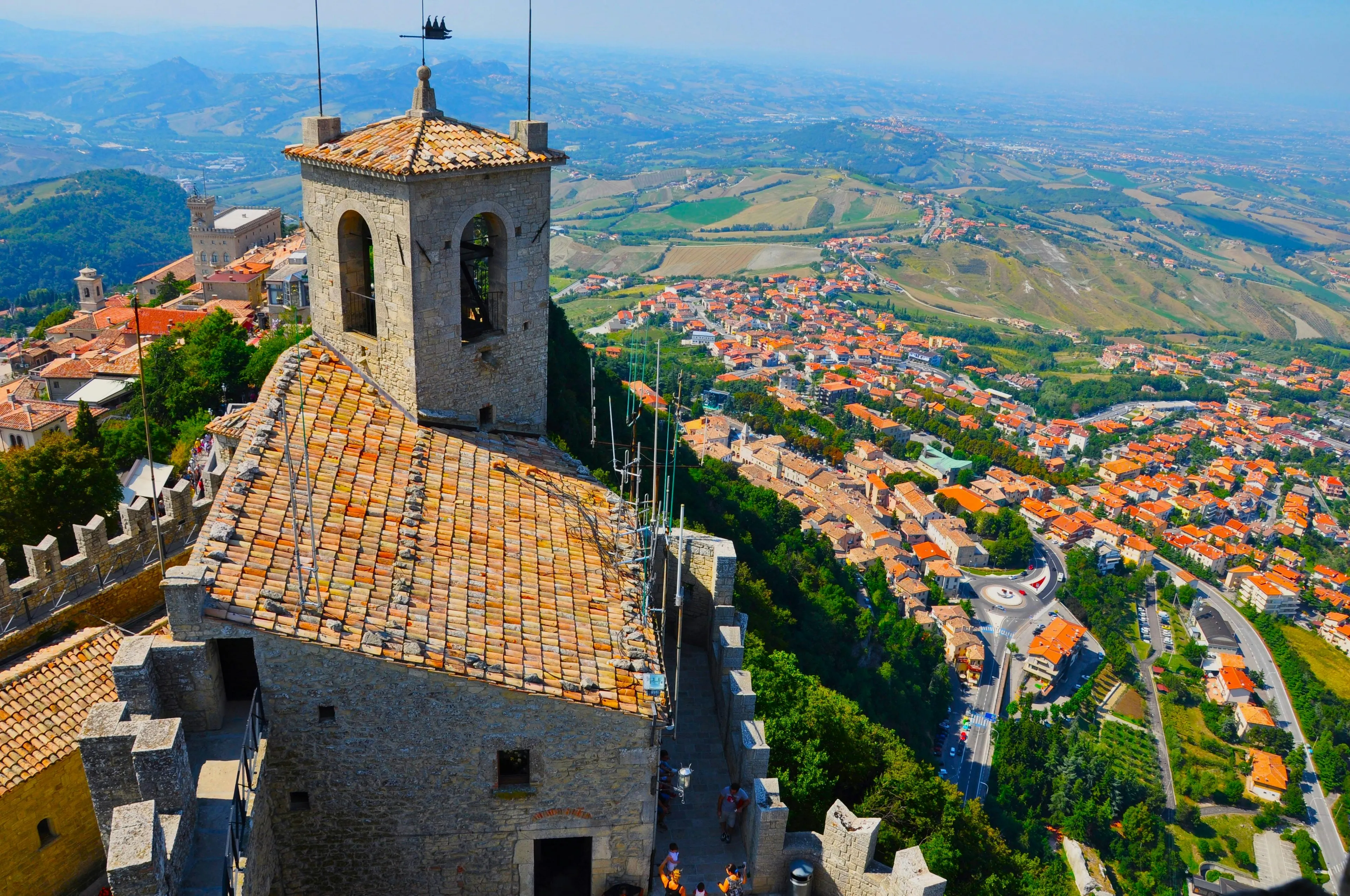 Scenic view of San Marino landscape with historic stone tower and red-roofed buildings surrounded by Italy countryside.