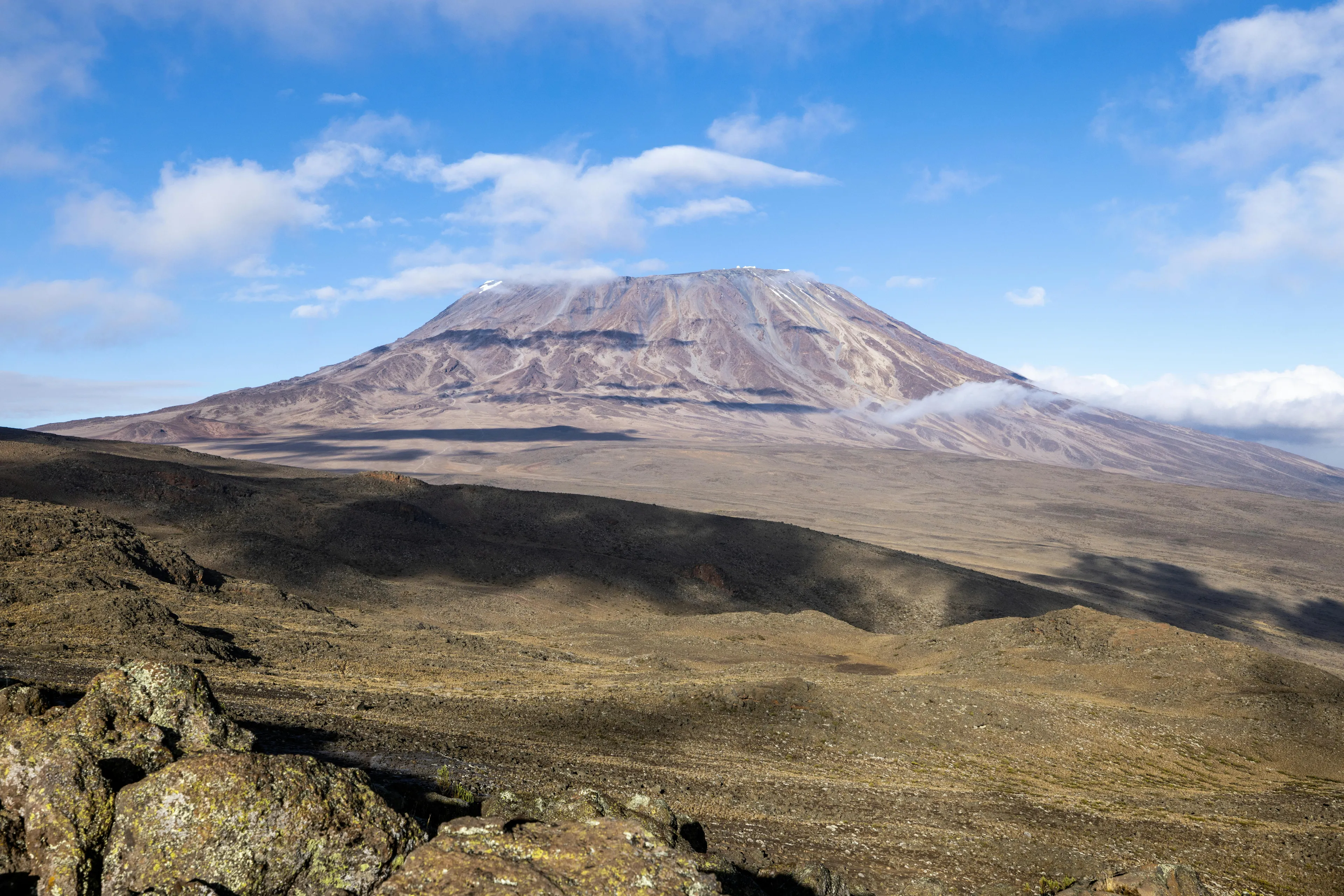 Mount Kilimanjaro towering over dry rugged terrain in the United Republic of Tanzania under a bright blue sky.