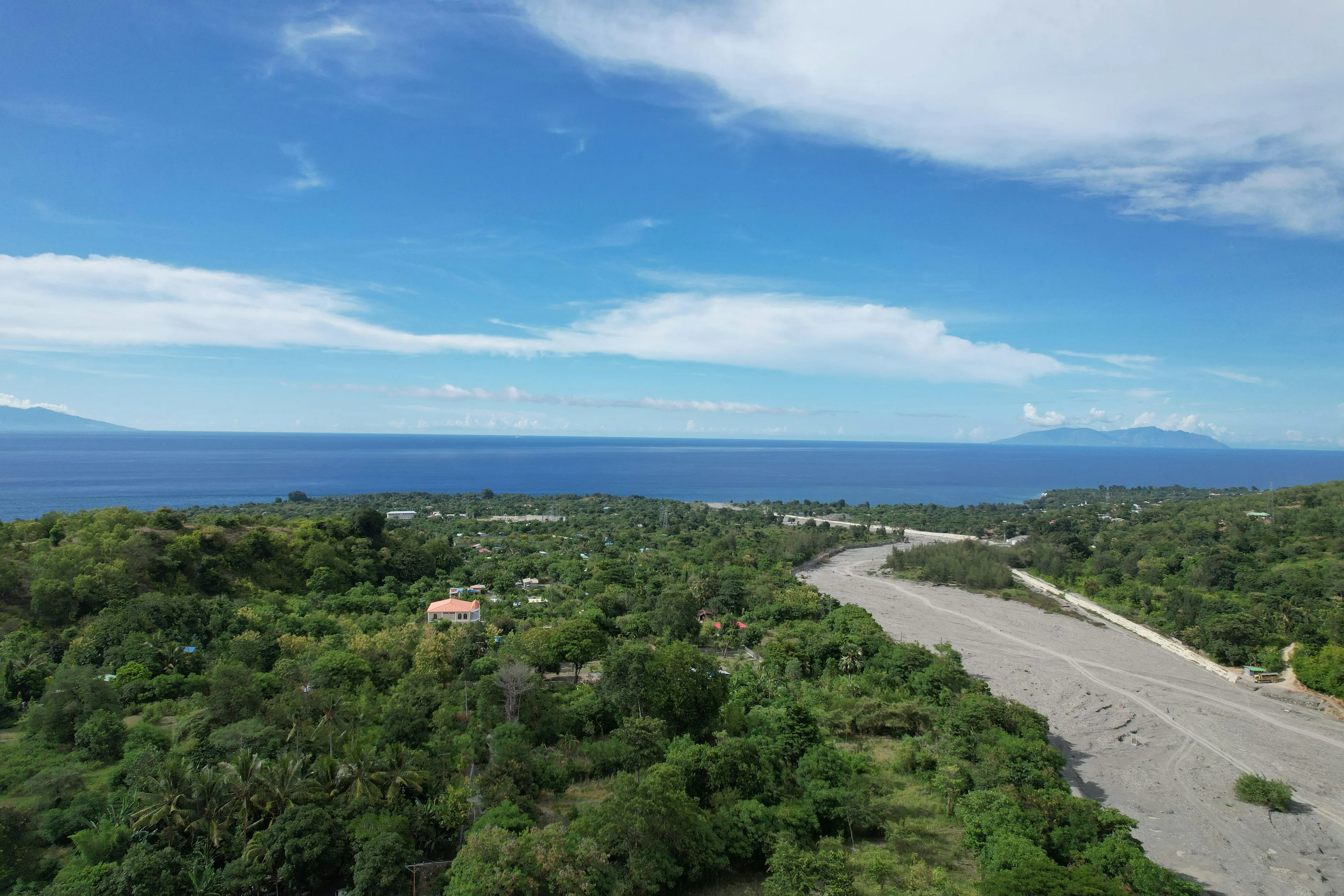 Aerial view of mountainous terrain and lush forests in the island nation of Timor-Leste with ocean and clear blue sky.
