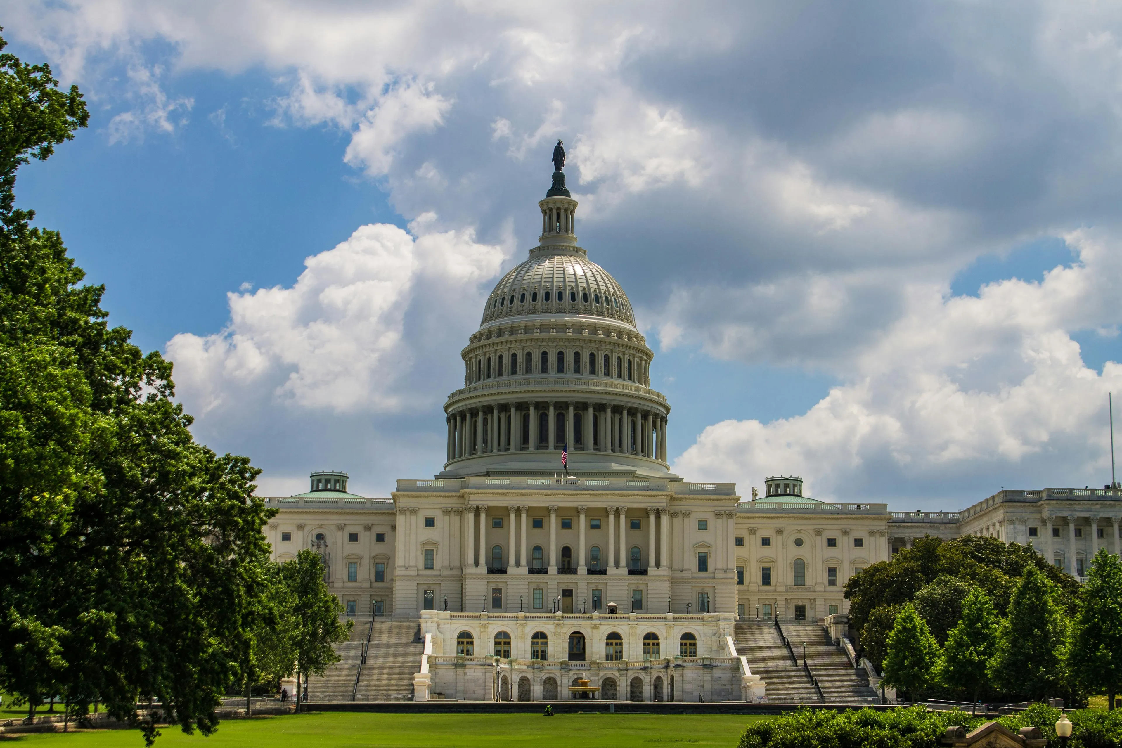 United States Capitol building in Washington DC with green trees and cloudy sky in the background, iconic US landmark.