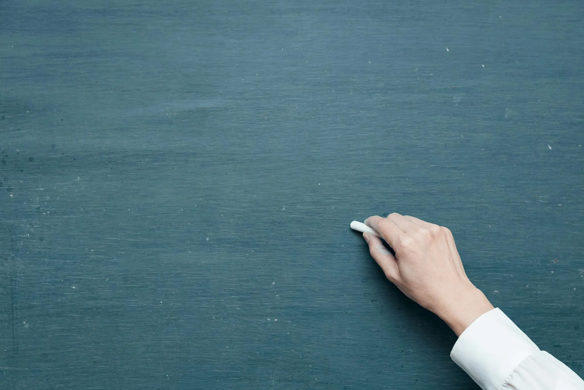 Hand holding a piece of chalk near a clean chalkboard in a classroom setting for grammar school questions.
