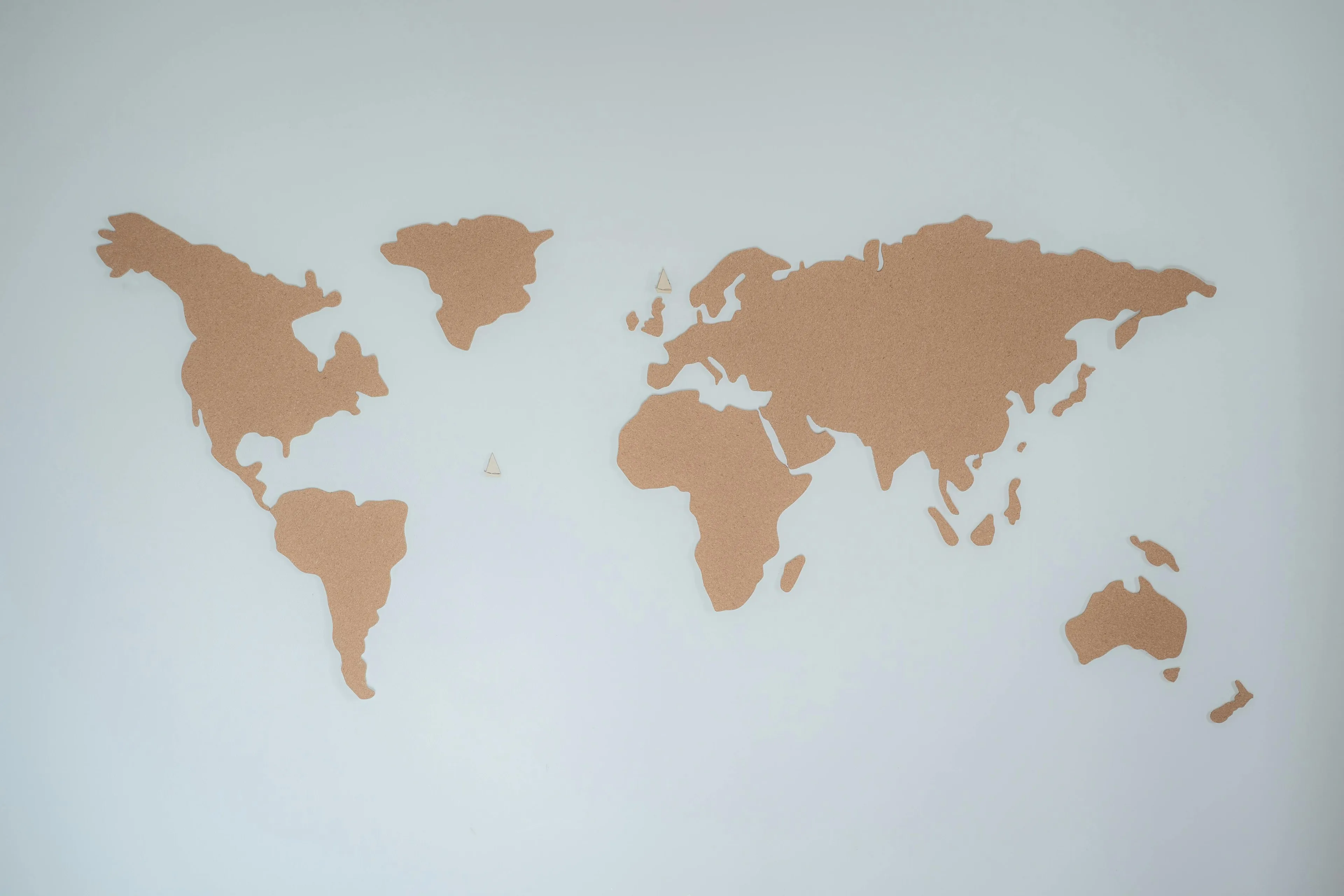 Cork board world map on white wall depicting continents, related to geography and continent countries question.
