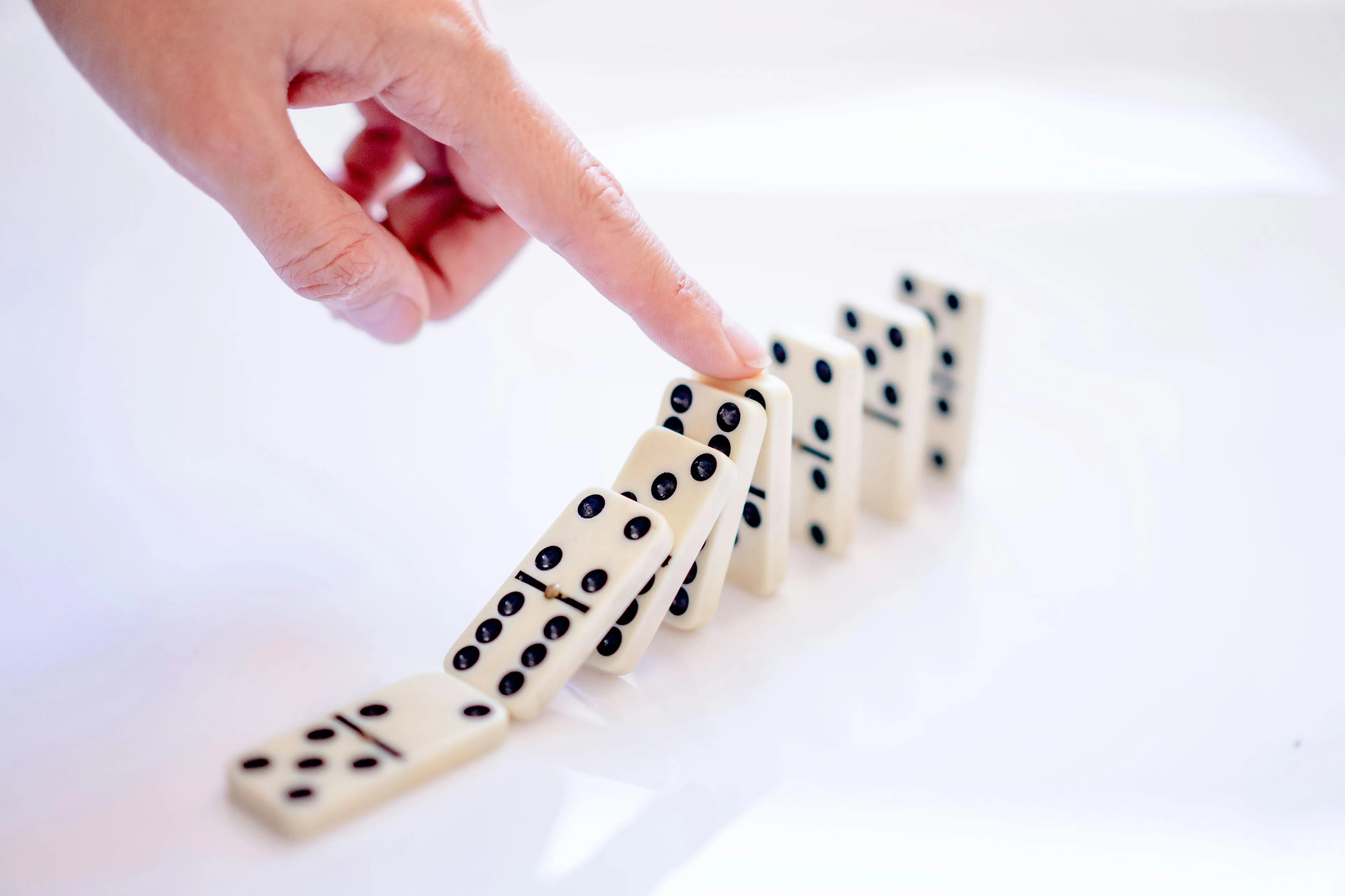 Finger pushing over domino pieces to show cause-and-effect concept for school questions and logic problem solving.