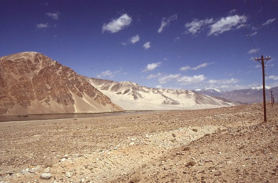 Arid landscape with mountains and power lines under a blue sky, representing the Silk Road important in ancient times.