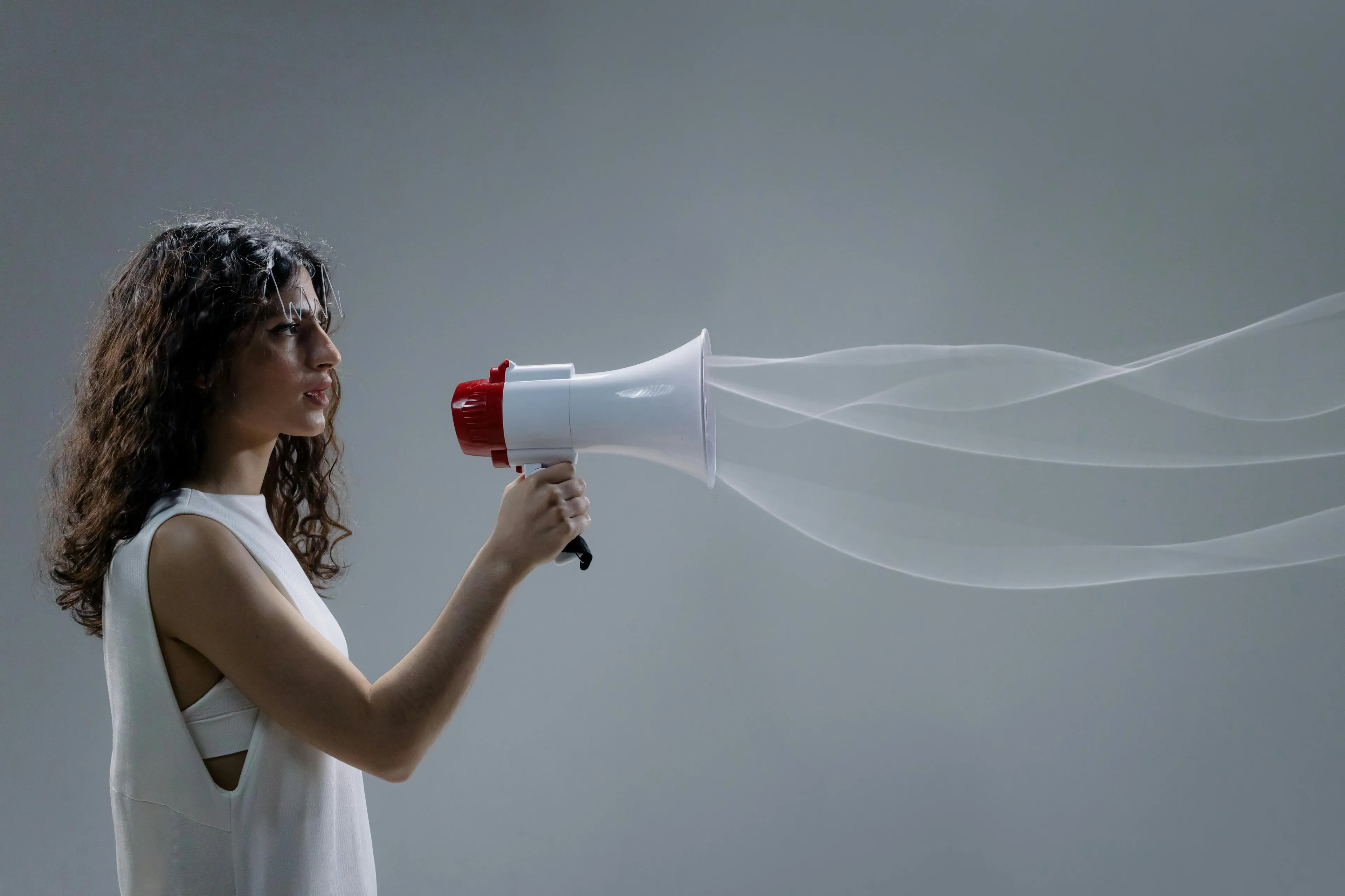 Young woman with curly hair holding a megaphone emitting sound waves illustrating frequency and pitch in physics.