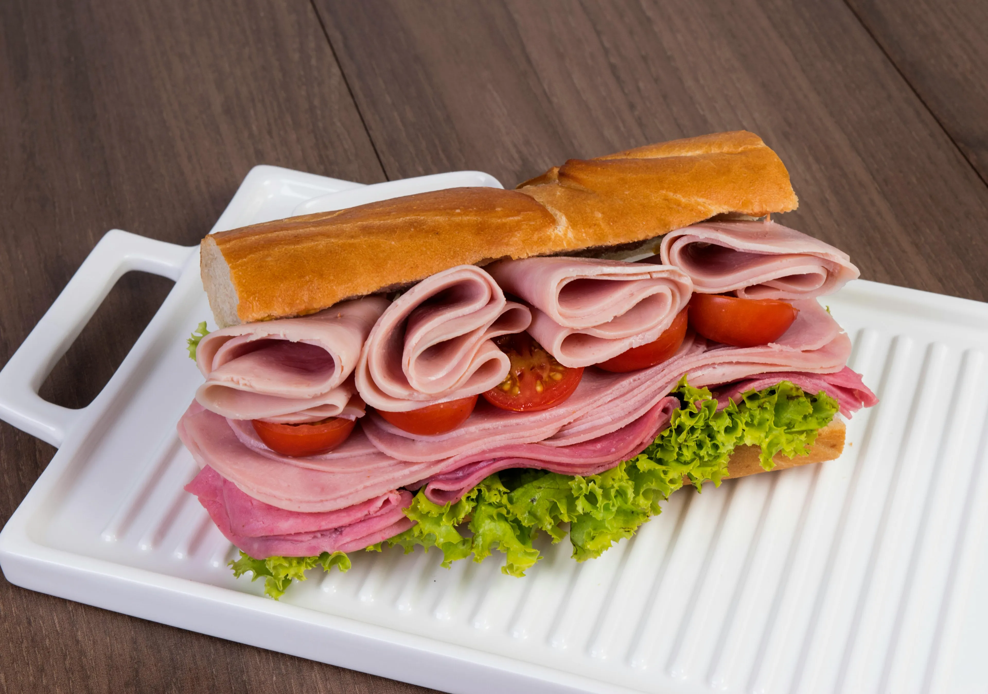 Sandwich with ham, lettuce, and tomato on white tray illustrating math discount price question.