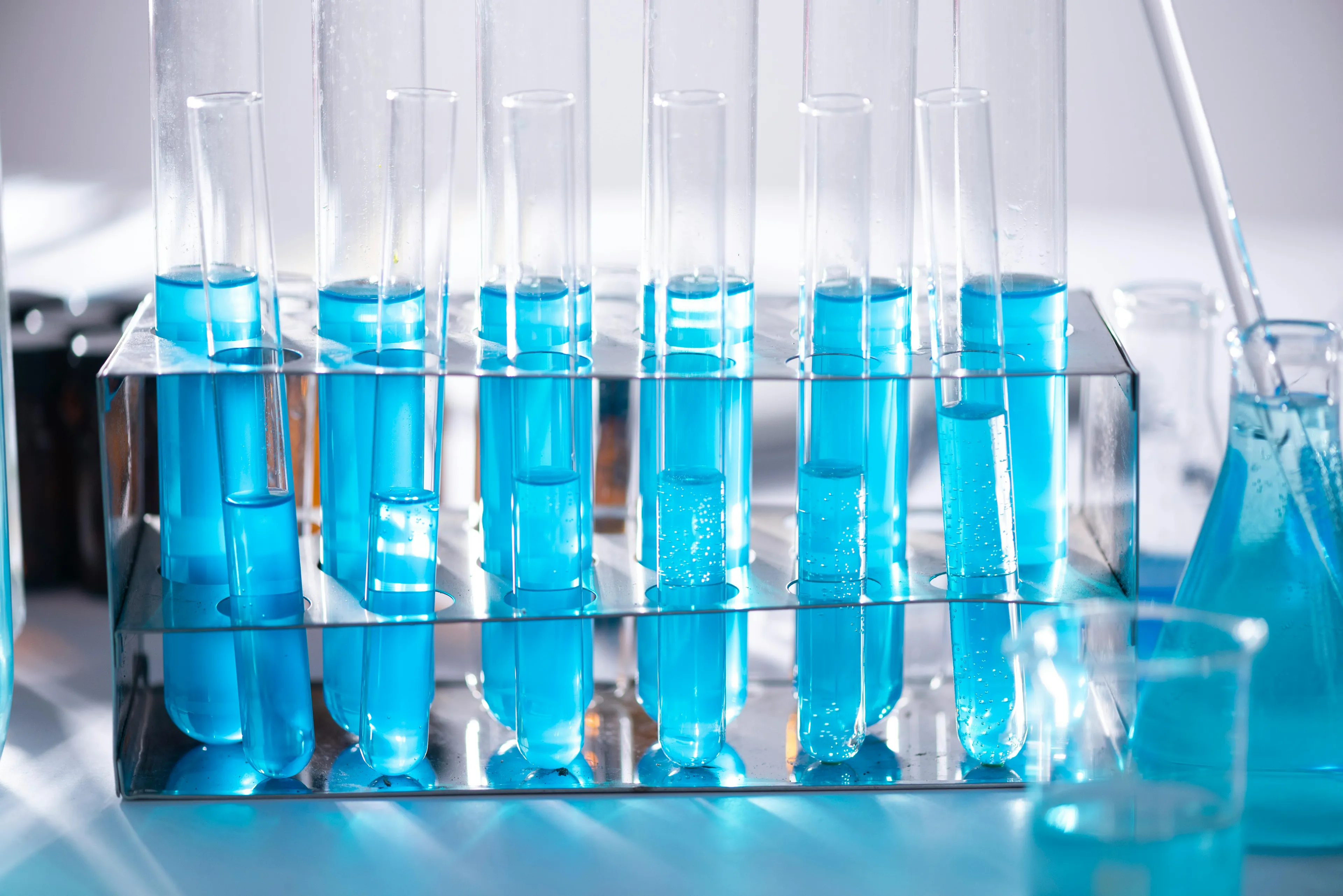 Test tubes filled with blue liquid in a rack for chemistry experiments testing substances with pH closest to neutral.