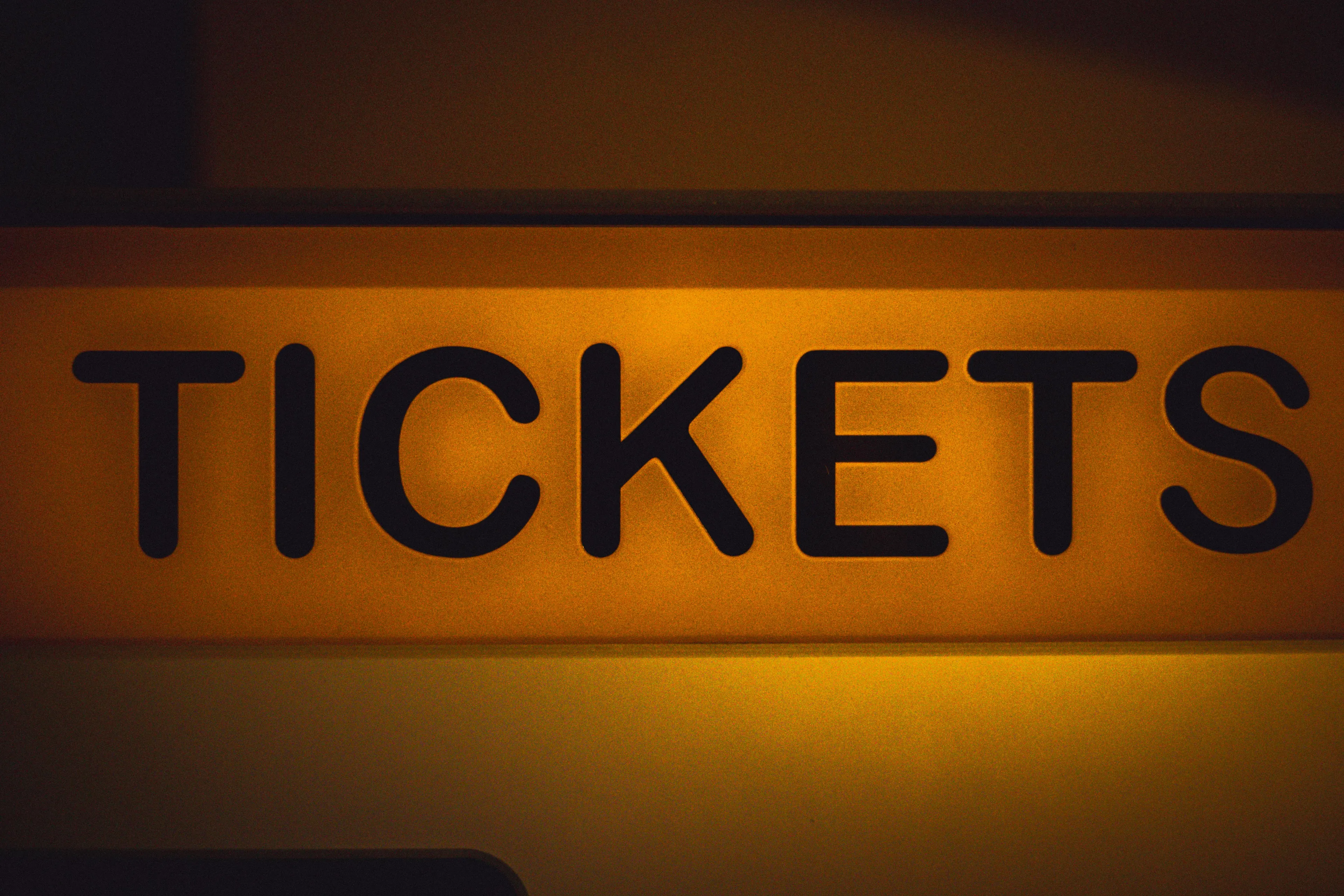 Illuminated movie theater tickets sign in black letters on a yellow background referencing ticket math problem.