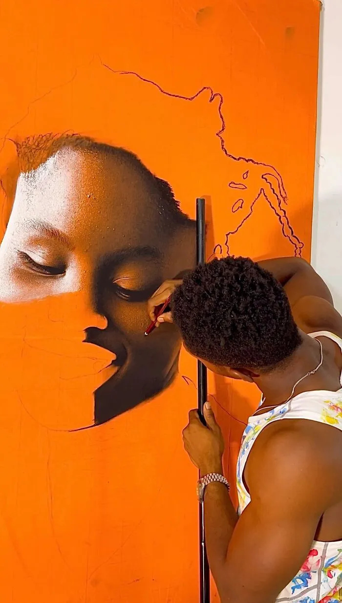 Artist creating a hyperrealistic portrait on an orange canvas, focusing on detailed facial features with a pencil.