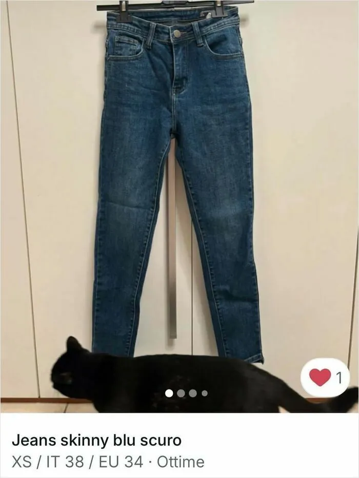 Black cat walking below a pair of skinny dark blue jeans in a Vinted clothing ad, spotlighting cats in ads.