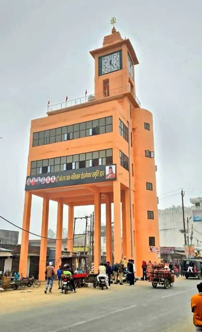 Orange clock tower on stilts in busy urban area, showcasing dystopian urban hell and the true price of modern life.