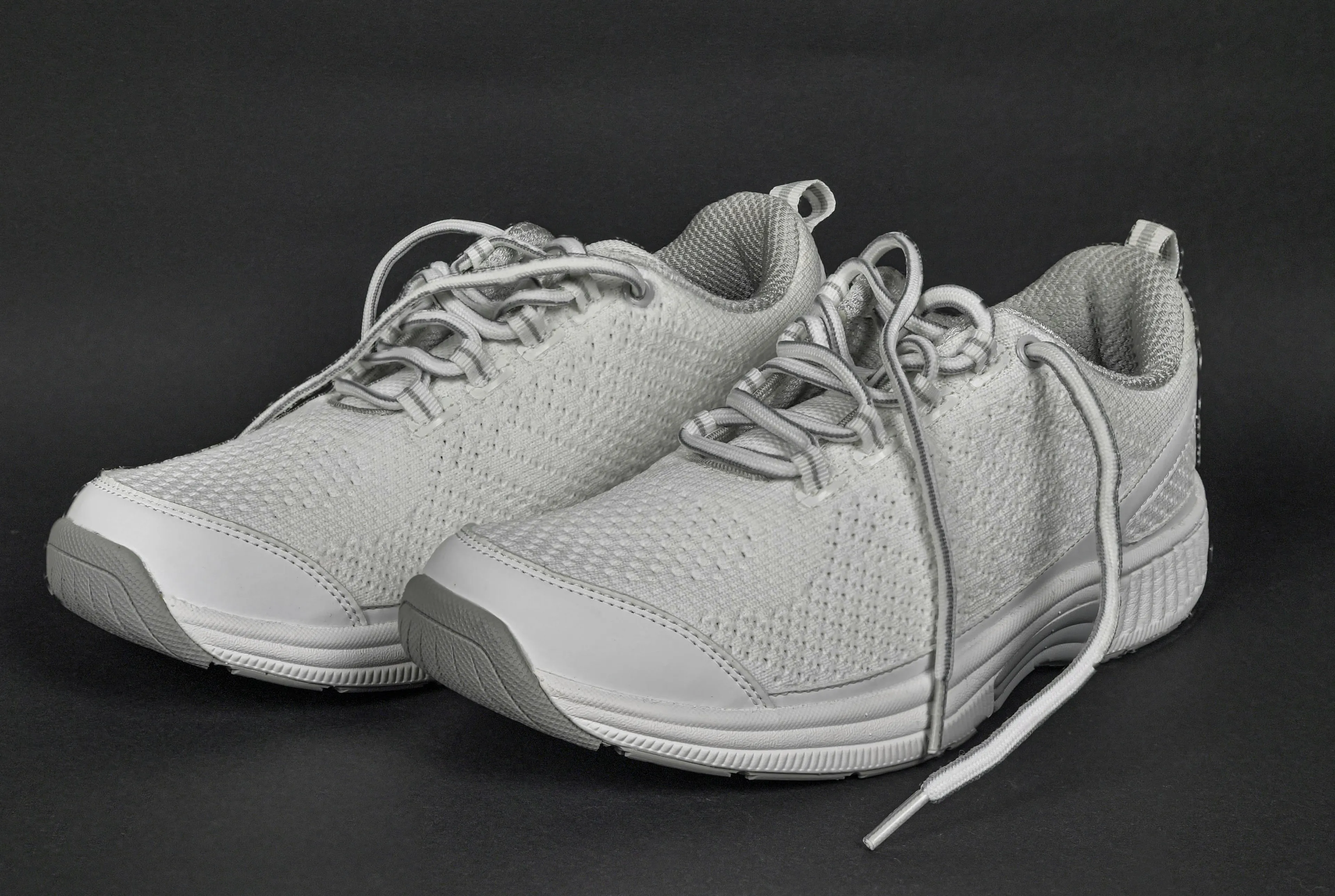 A pair of white sneakers with laces on a dark background, highlighting the timeless fashion accessory trend.