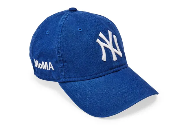 Blue baseball cap with white New York Yankees logo and MoMA text, showcasing a popular decades-defining fashion accessory.