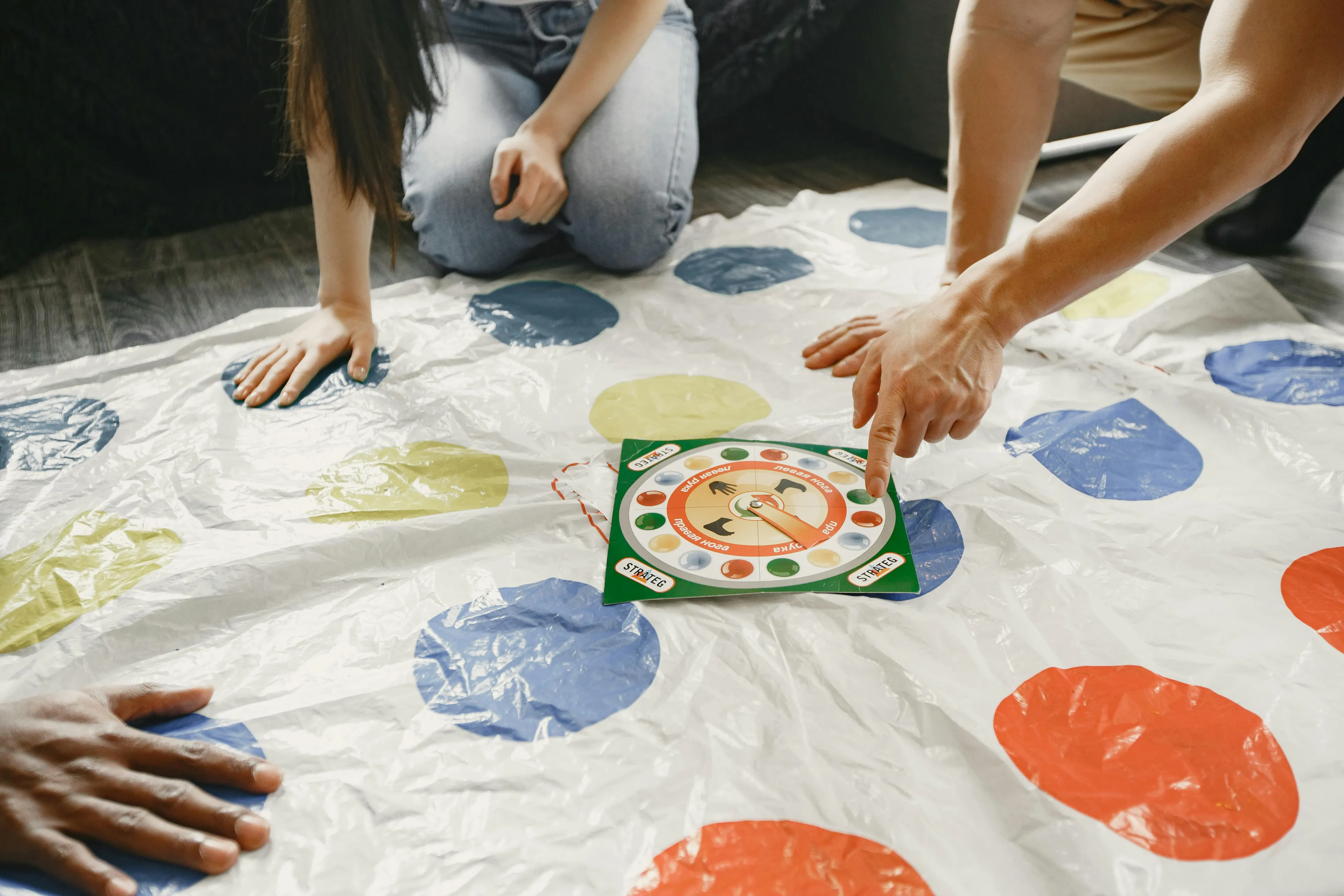 Players placing hands on colored spots of a Twister mat while spinning the game spinner during playtime.