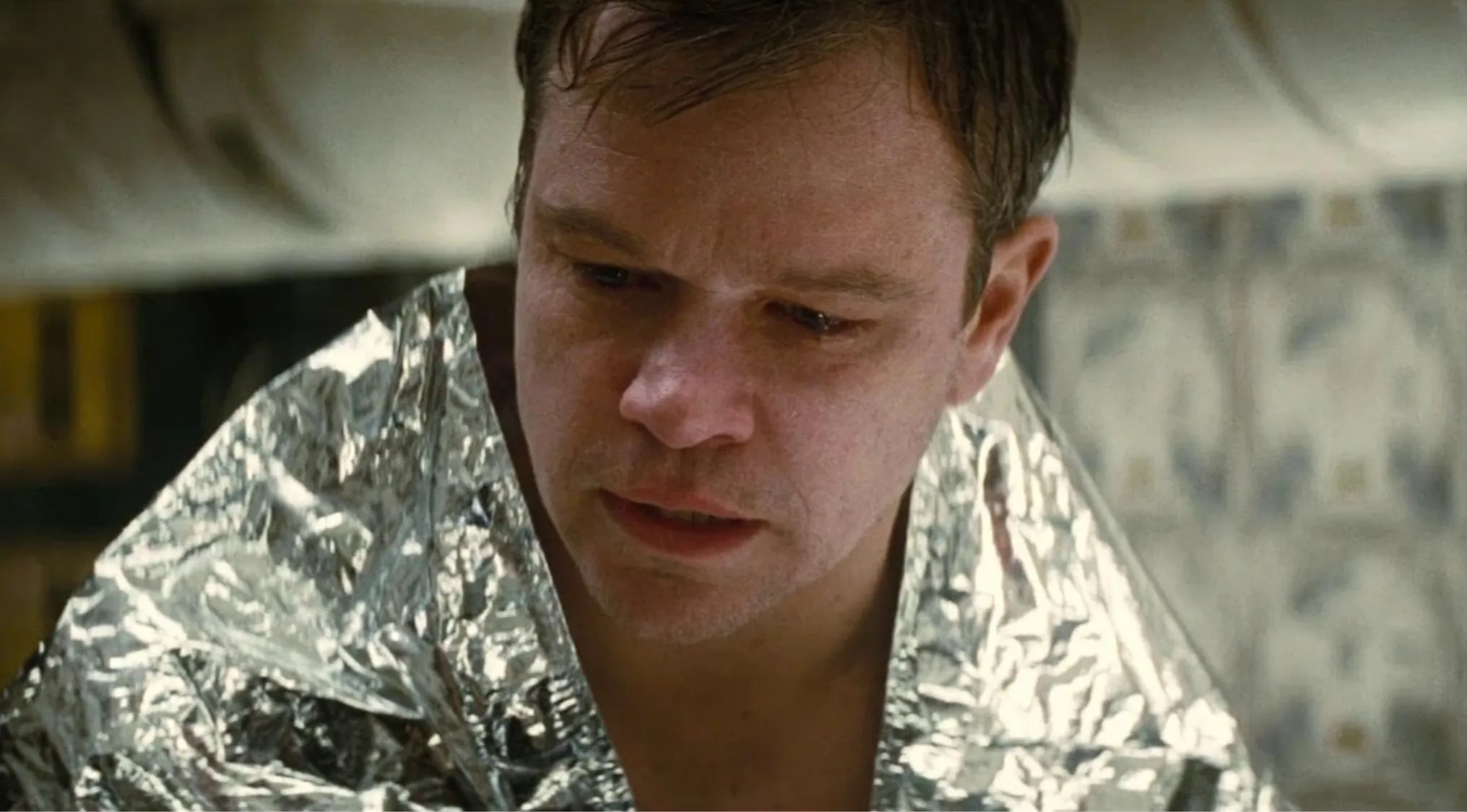 Side character from Interstellar wrapped in a foil blanket, showing a distressed and focused expression indoors.