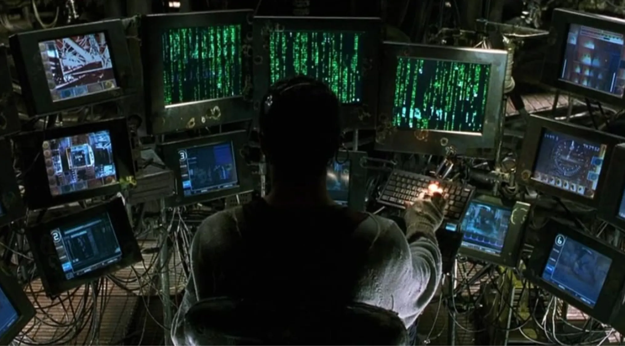 Side character Cypher operating multiple computer monitors displaying green Matrix code in a dark control room.