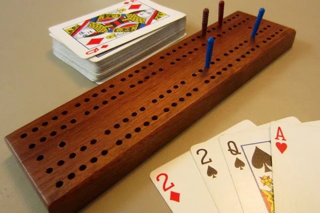 Wooden cribbage board with pegs and playing cards including 2, queen, and ace for a classic board game night.