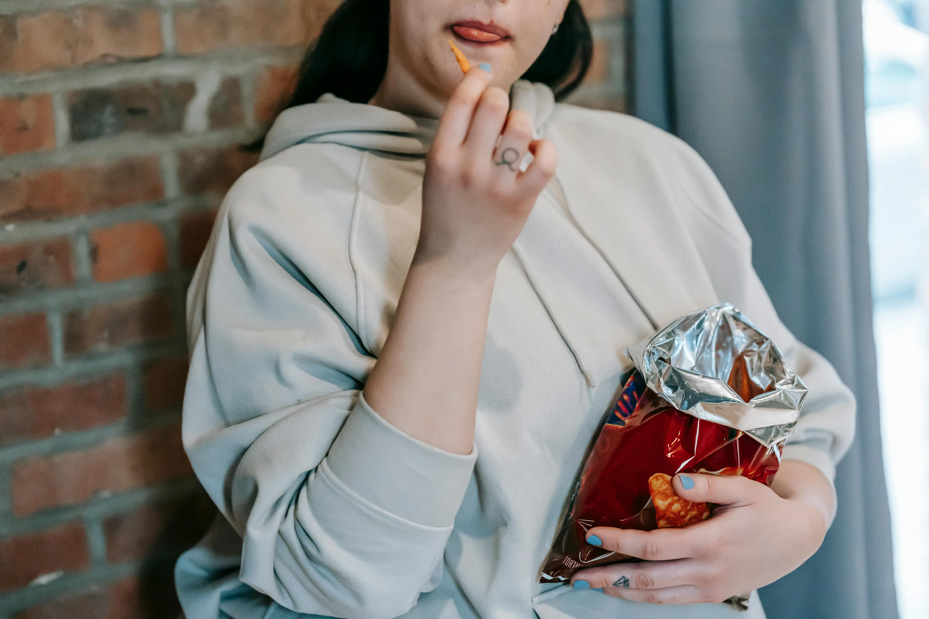 Person in a hoodie eating crunchy snack from an open bag, illustrating which sitcom snack saves the day at 11 PM.