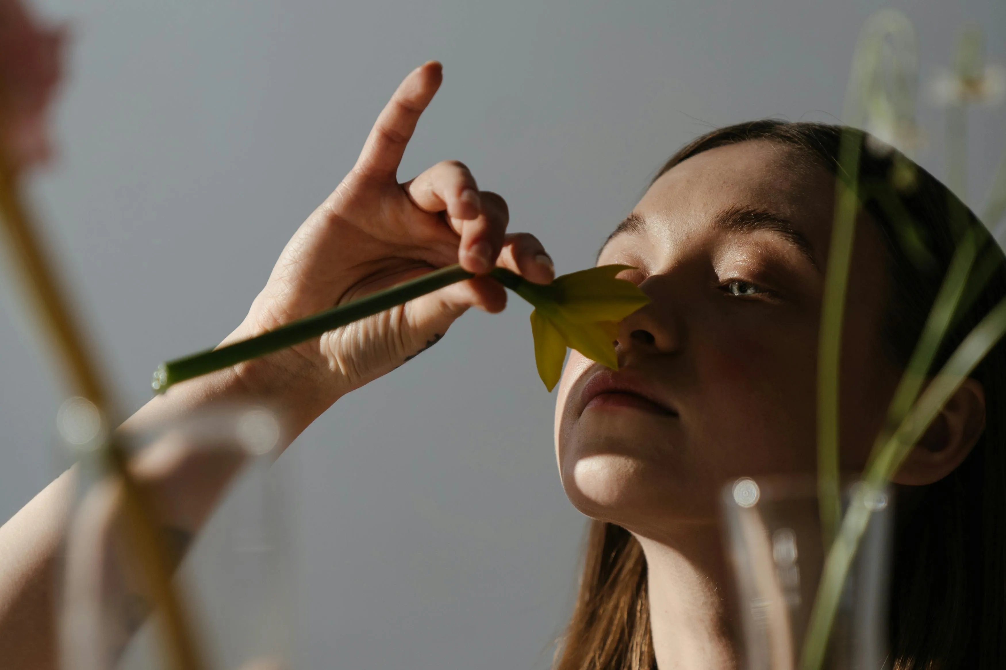 Young woman smelling a yellow flower, exploring which out of these smells is the best in a thoughtful moment.