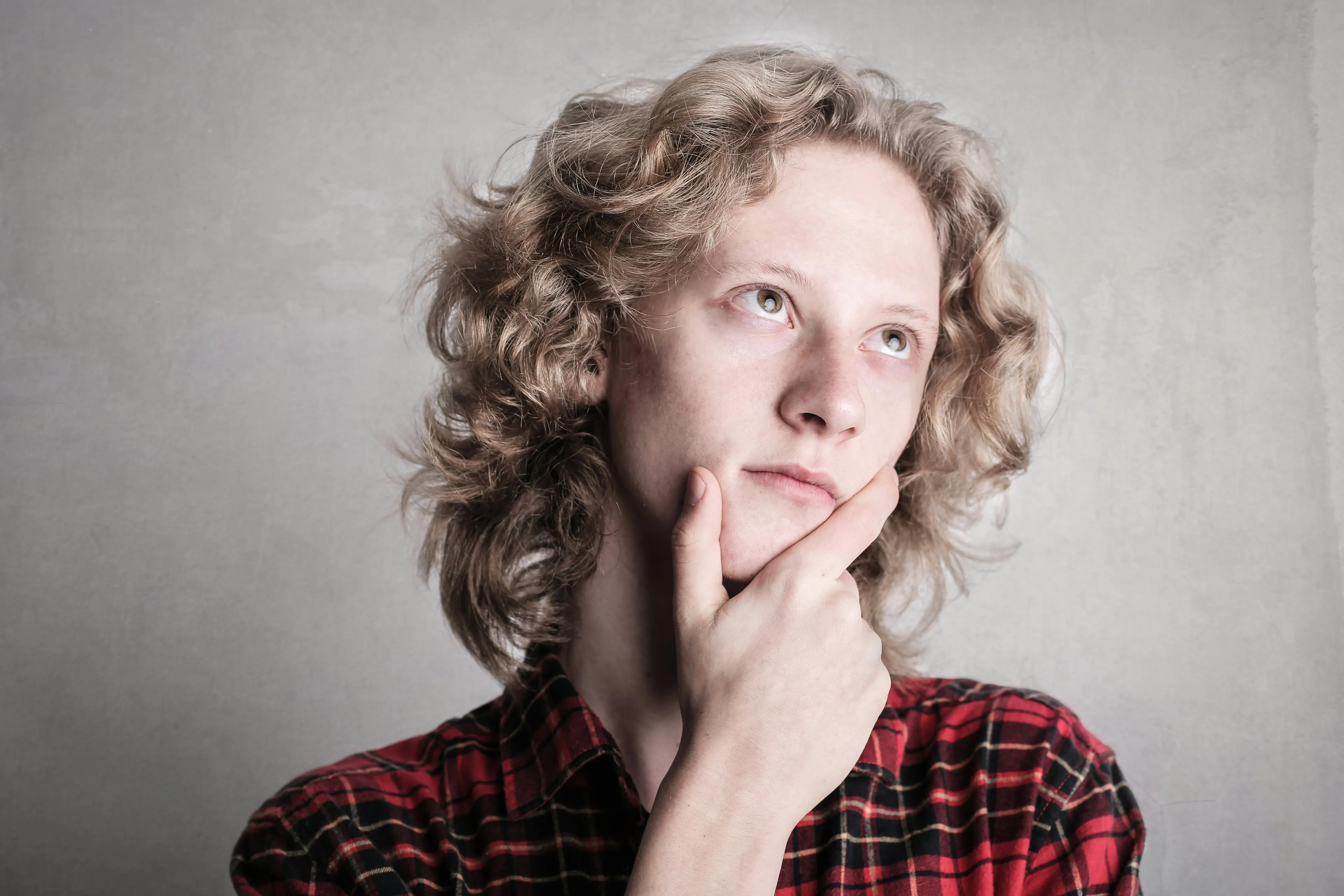 Young person in red plaid shirt thoughtfully considering which sitcom they belong in with a curious expression.