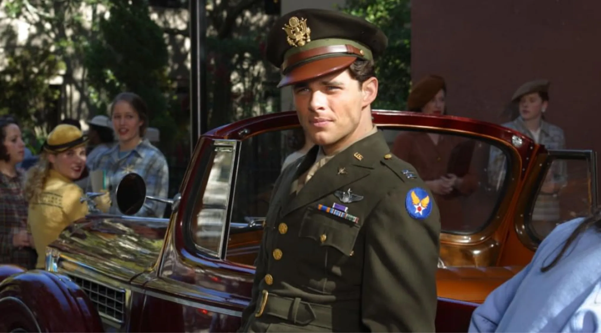 Side character from The Notebook in military uniform standing near a vintage car with people in the background.