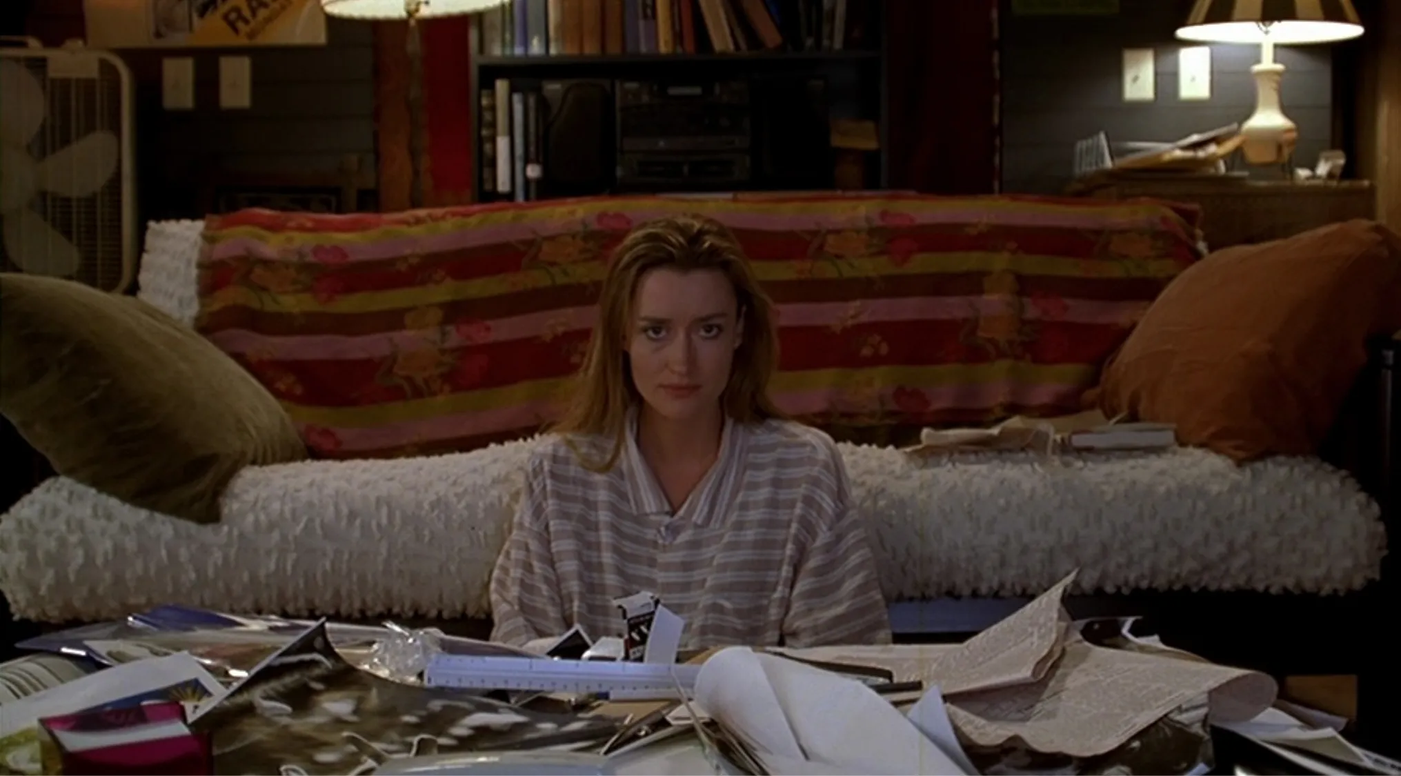 Side character from The Truman Show sitting with papers and books scattered in front in a cozy living room setting.