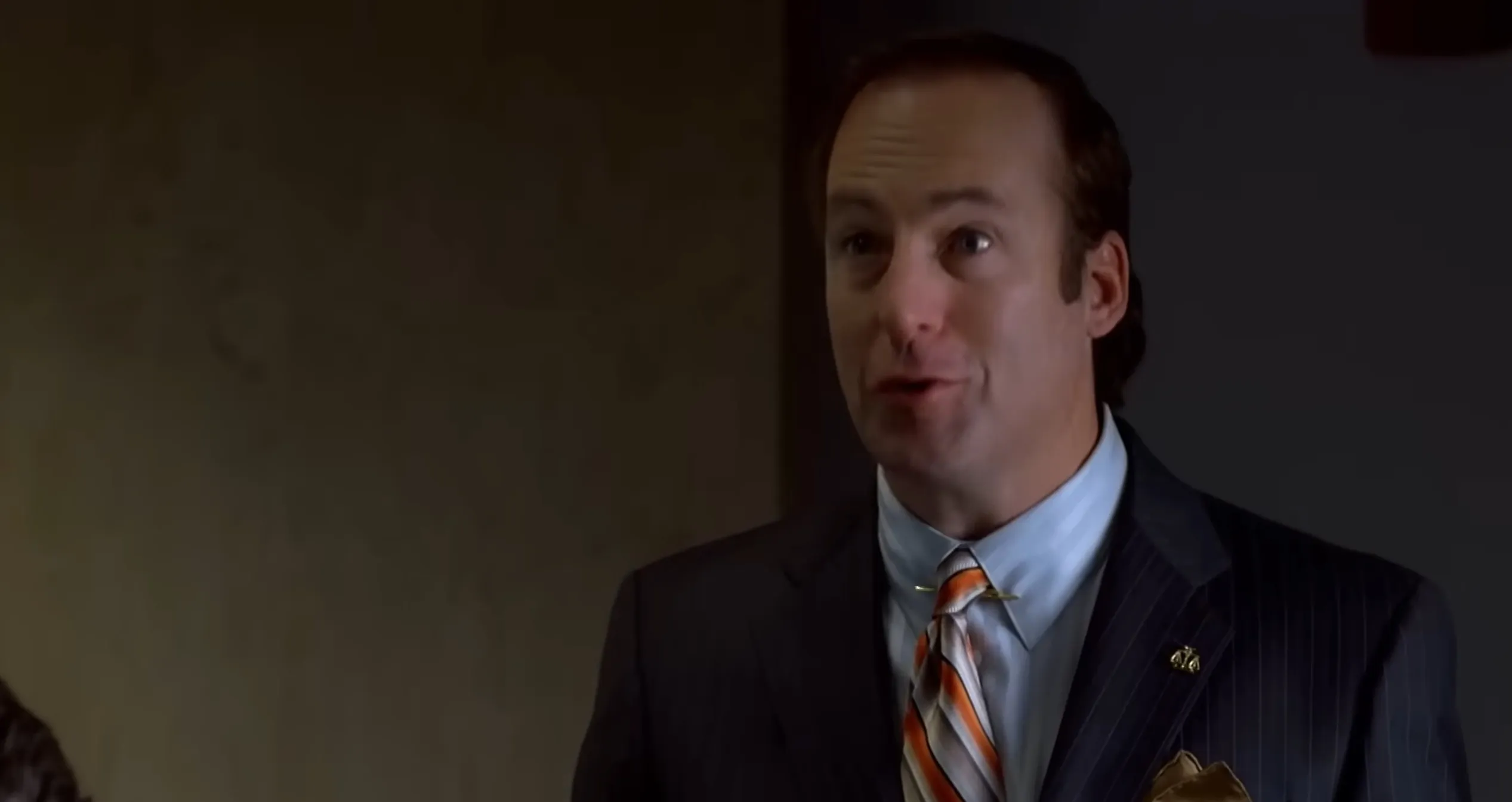 Man in suit with striped tie and lapel pin speaking, guess the supporting character from TV show quiz.