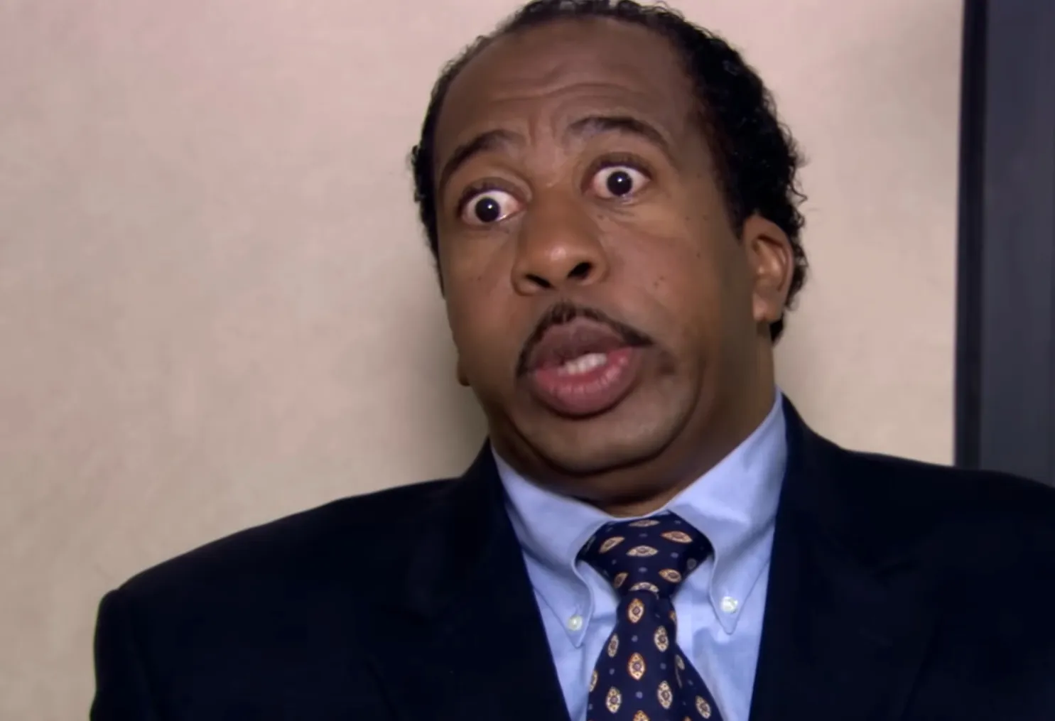 Stanley from The Office wearing a suit and tie with a surprised expression as Quality Control Representative.