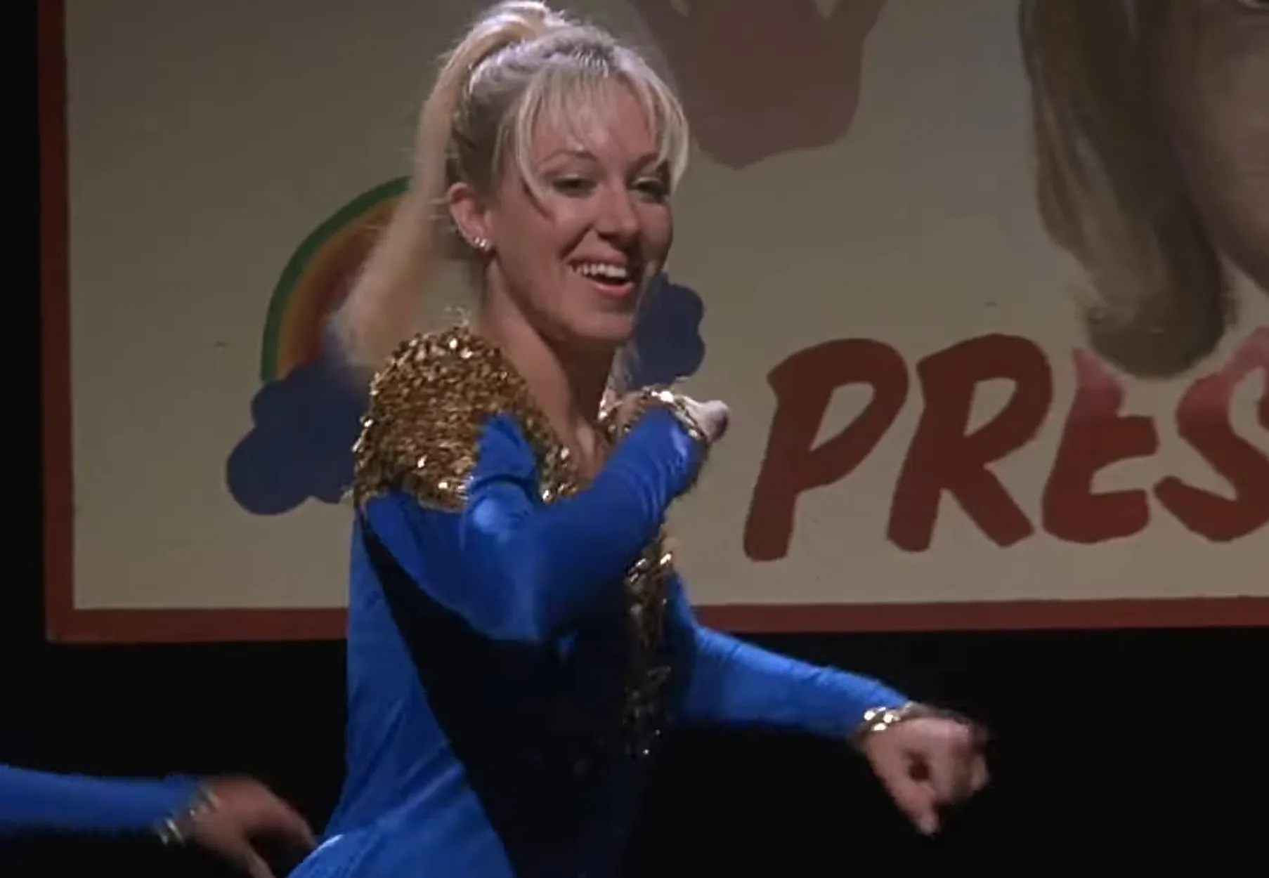 Female cheerleader in a blue and gold outfit performing on stage related to Rico uncle character in Napoleon Dynamite summer