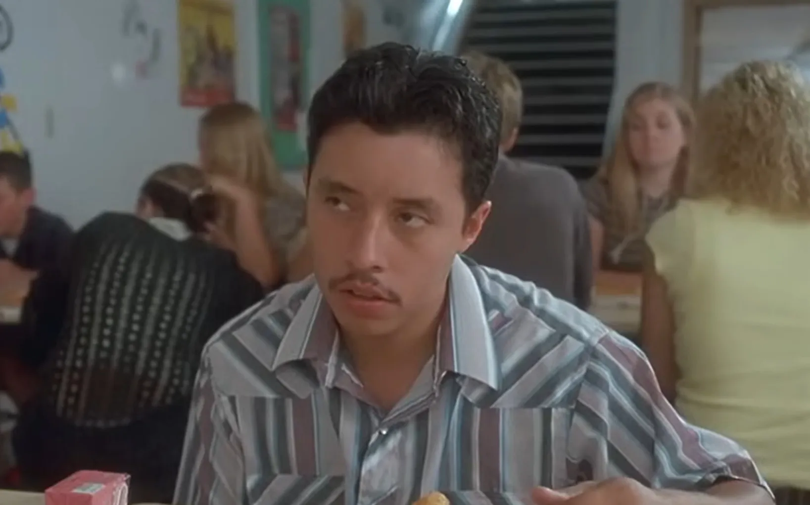 Pedro sitting in a cafeteria scene from Napoleon Dynamite, character shown wearing a striped shirt and mustache.