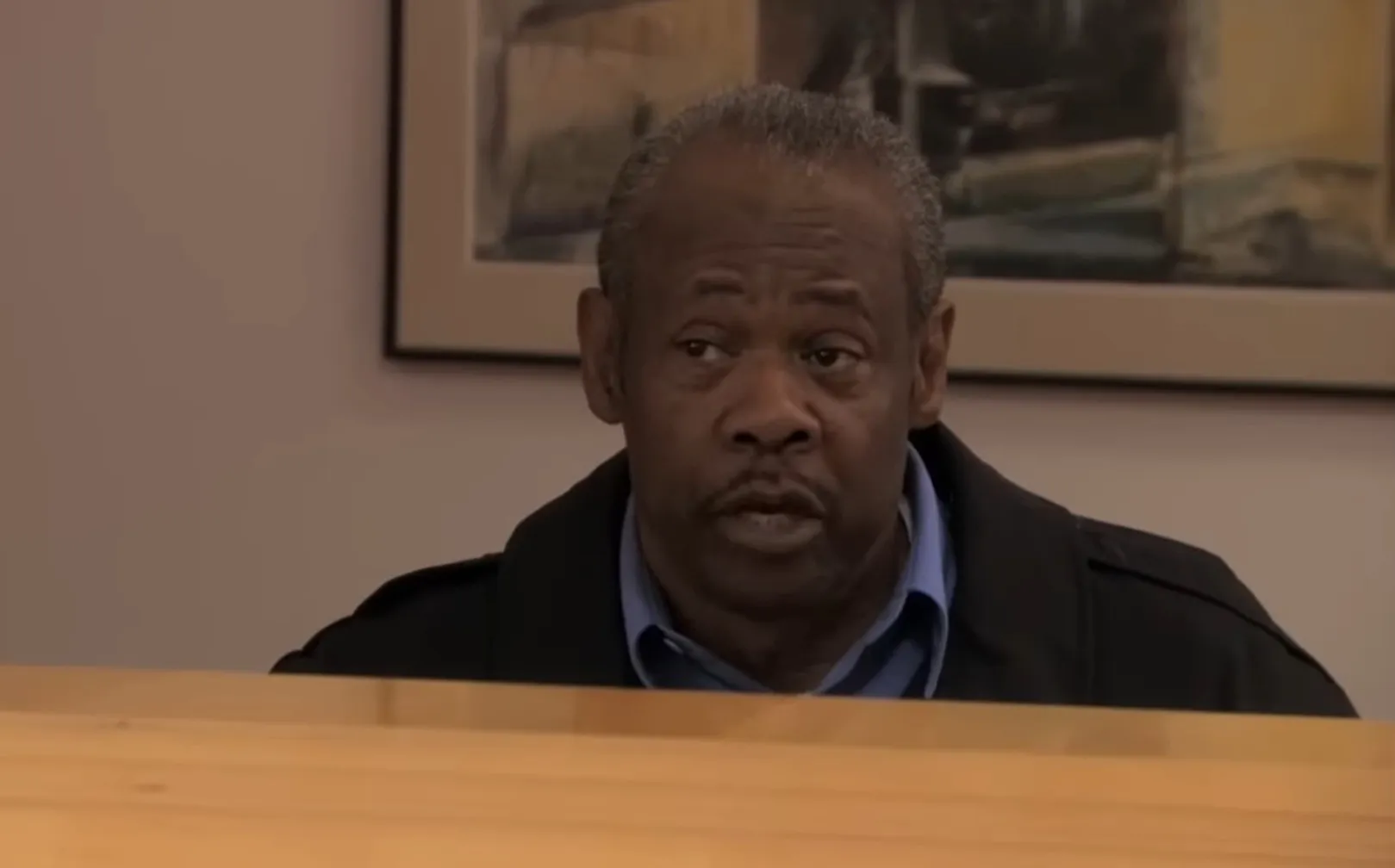 Hank as the Quality Control Representative in The Office, sitting at a desk with a serious expression.