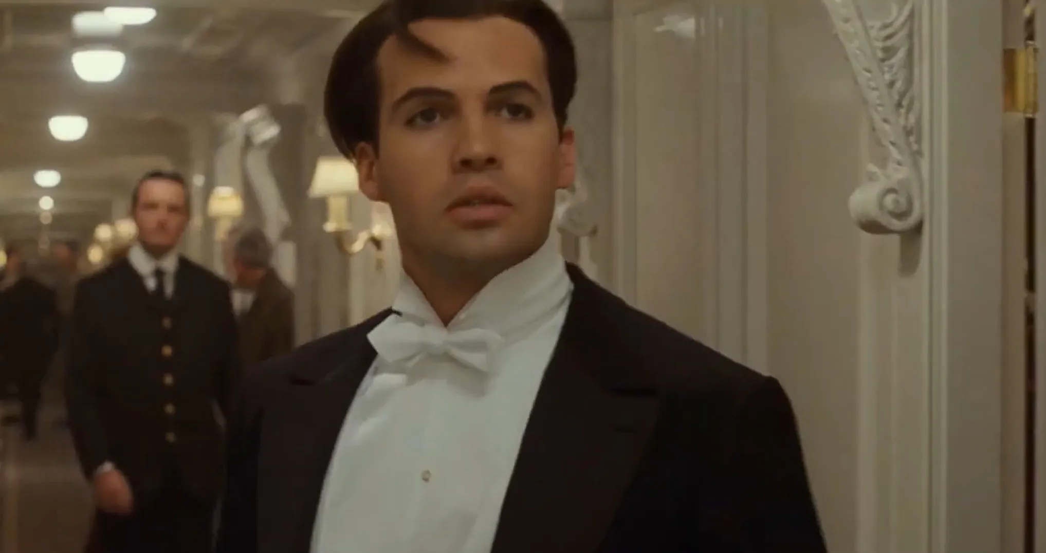 Supporting character on Titanic in formal attire walking through a hallway during a scene from the movie.