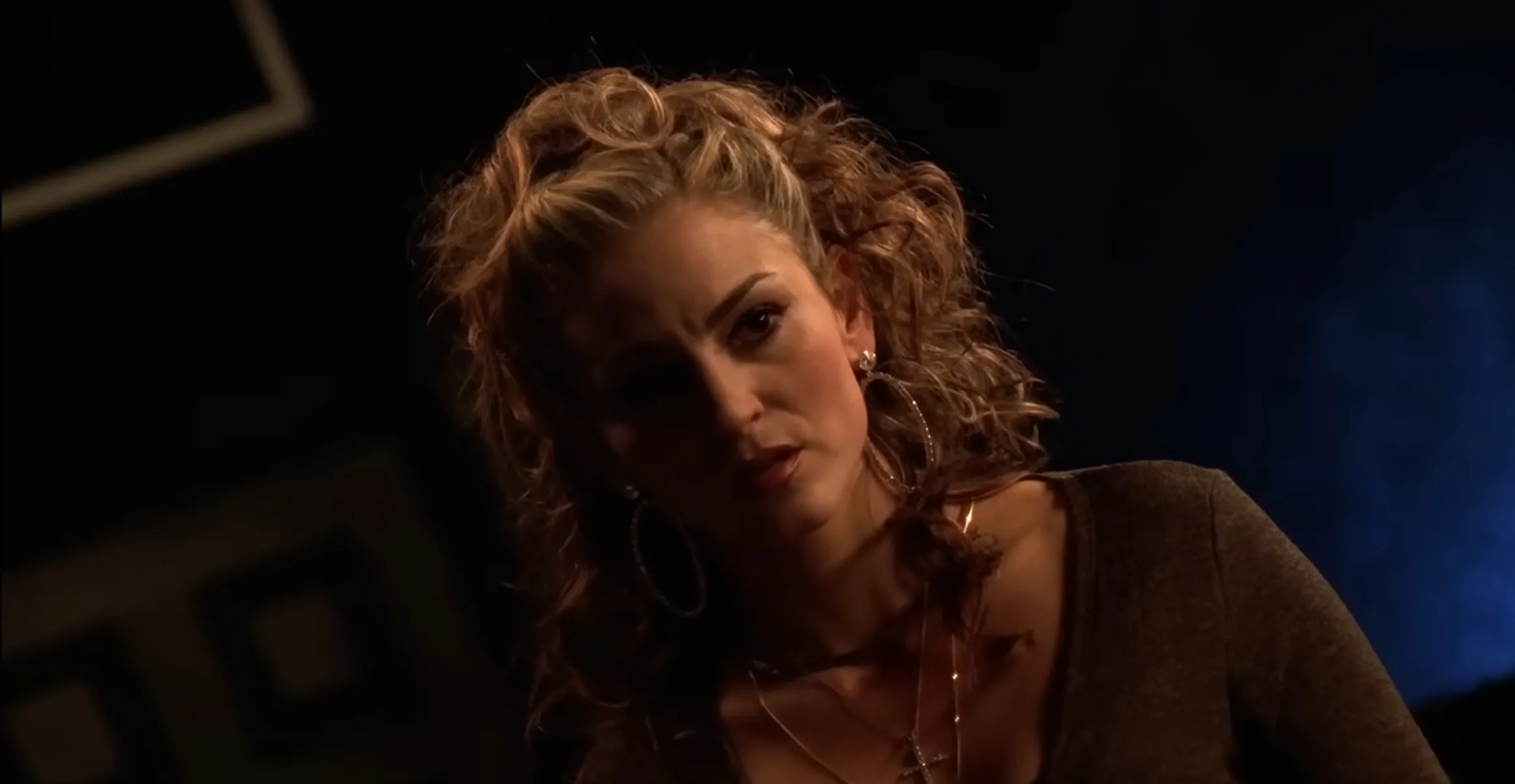 Adriana in The Sopranos with curly hair and hoop earrings in a dark, dramatic setting representing a supporting character role.