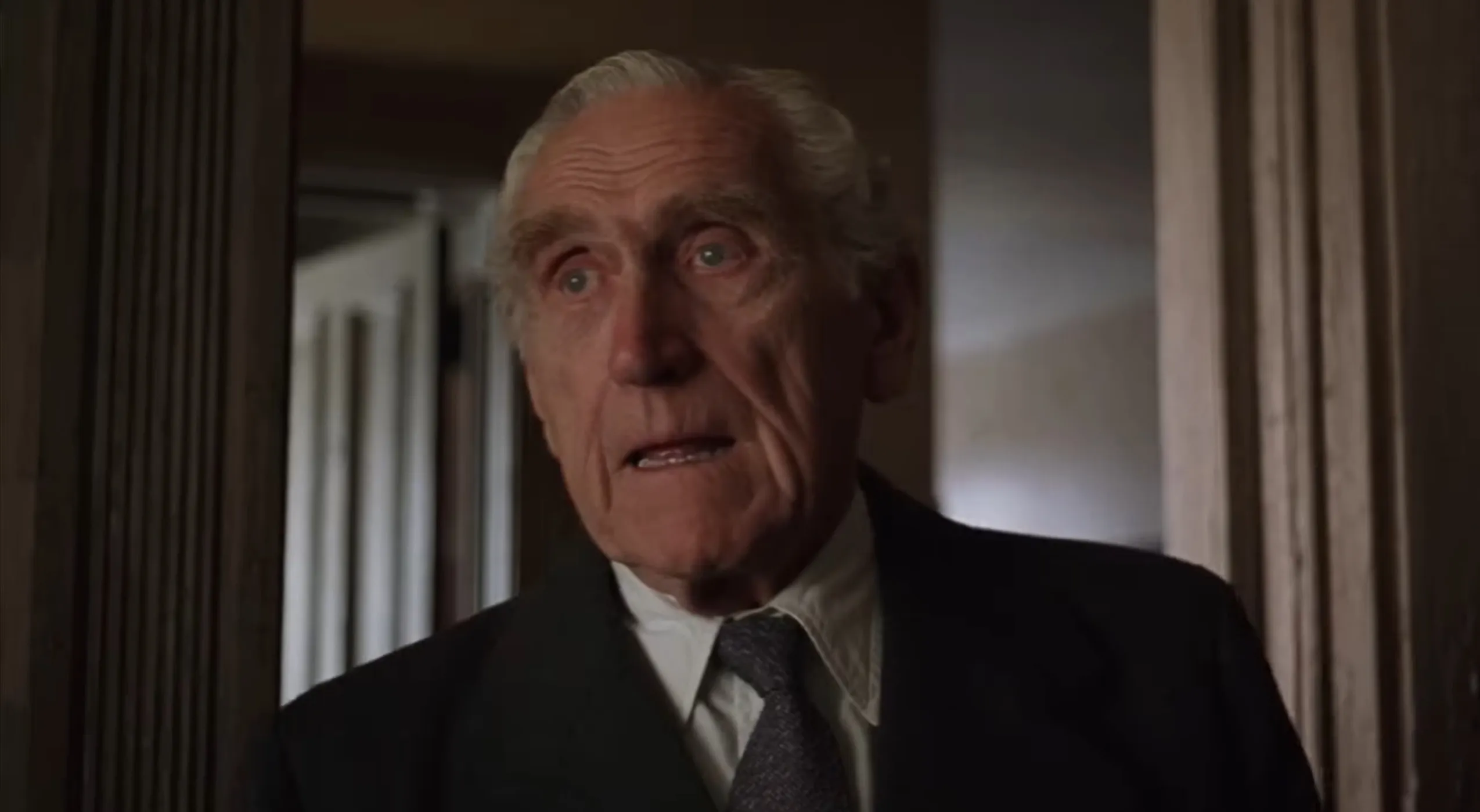 Elderly supporting character from Shawshank Redemption wearing a suit and tie in a dimly lit room.