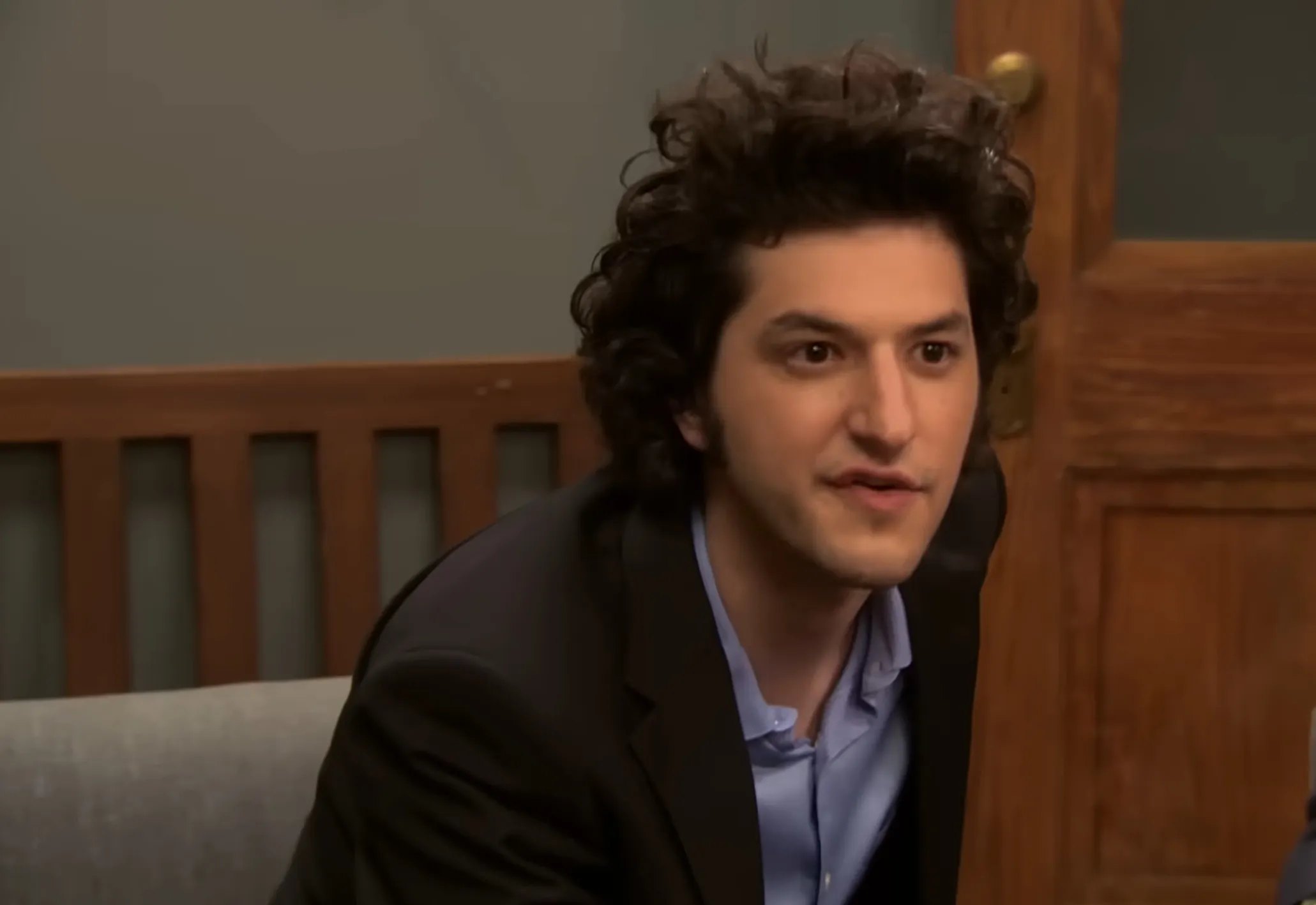 Jean-Ralphio Saperstein from Parks and Recreation sitting indoors wearing a black jacket and blue shirt.